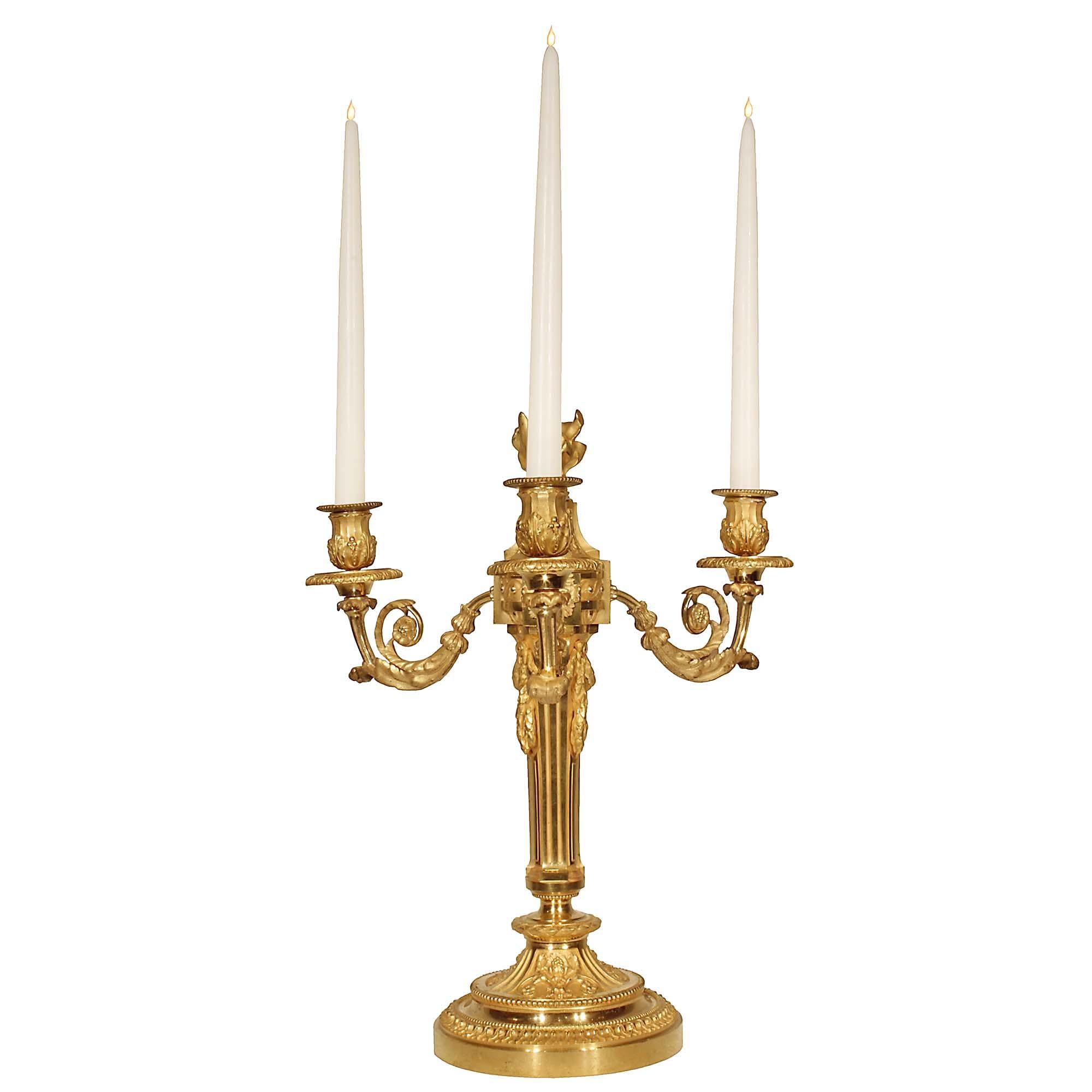 An elegant pair of French 19 century Louis XVI st. three arm ormolu candelabras. Each candelabra is raised on a circular base decorated with sensational and richly chased foliate patterns in a satin and burnished finish. The central fut has a fluted