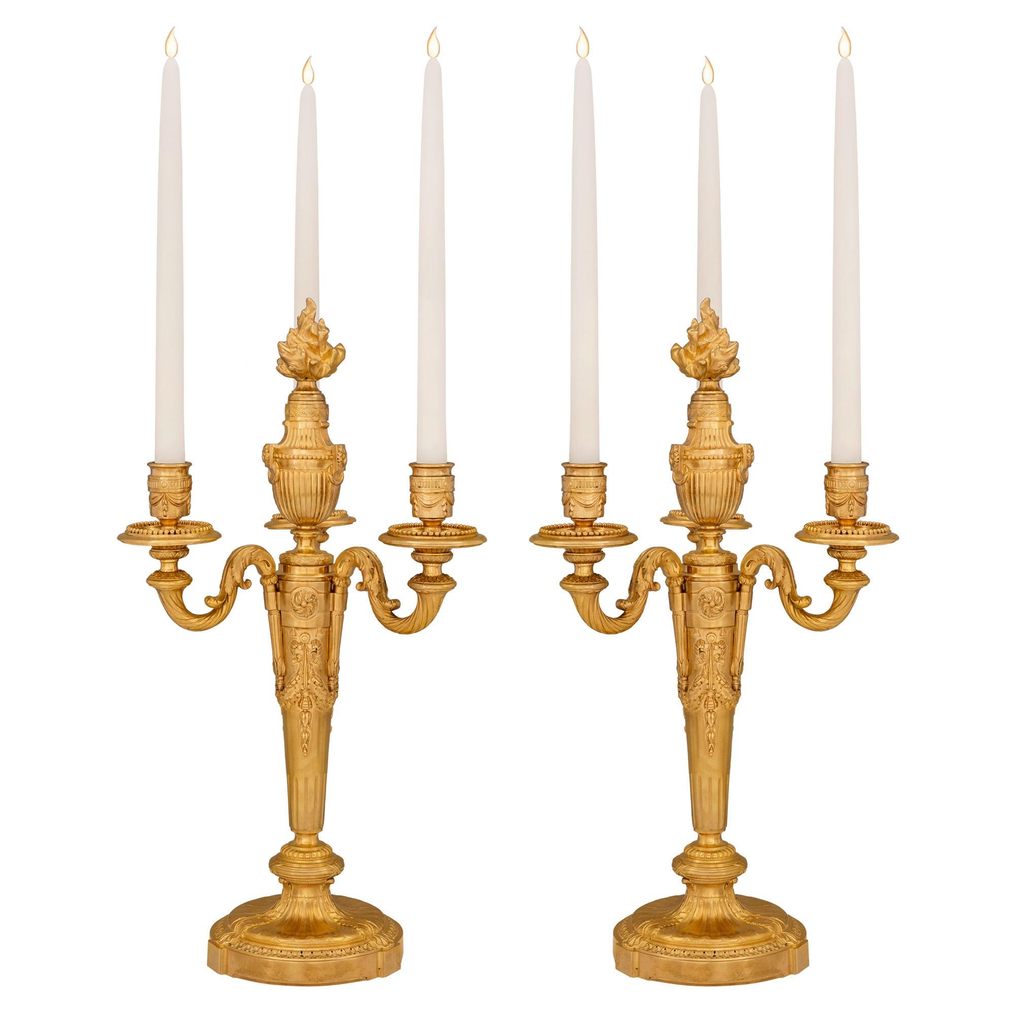 A most elegant pair of French 19th century Louis XVI st. ormolu candelabras. Each three arm candelabra is raised by a fine circular base with a detailed Coeur de Rai wrap around band and acanthus leaves. The tapered central supports display richly