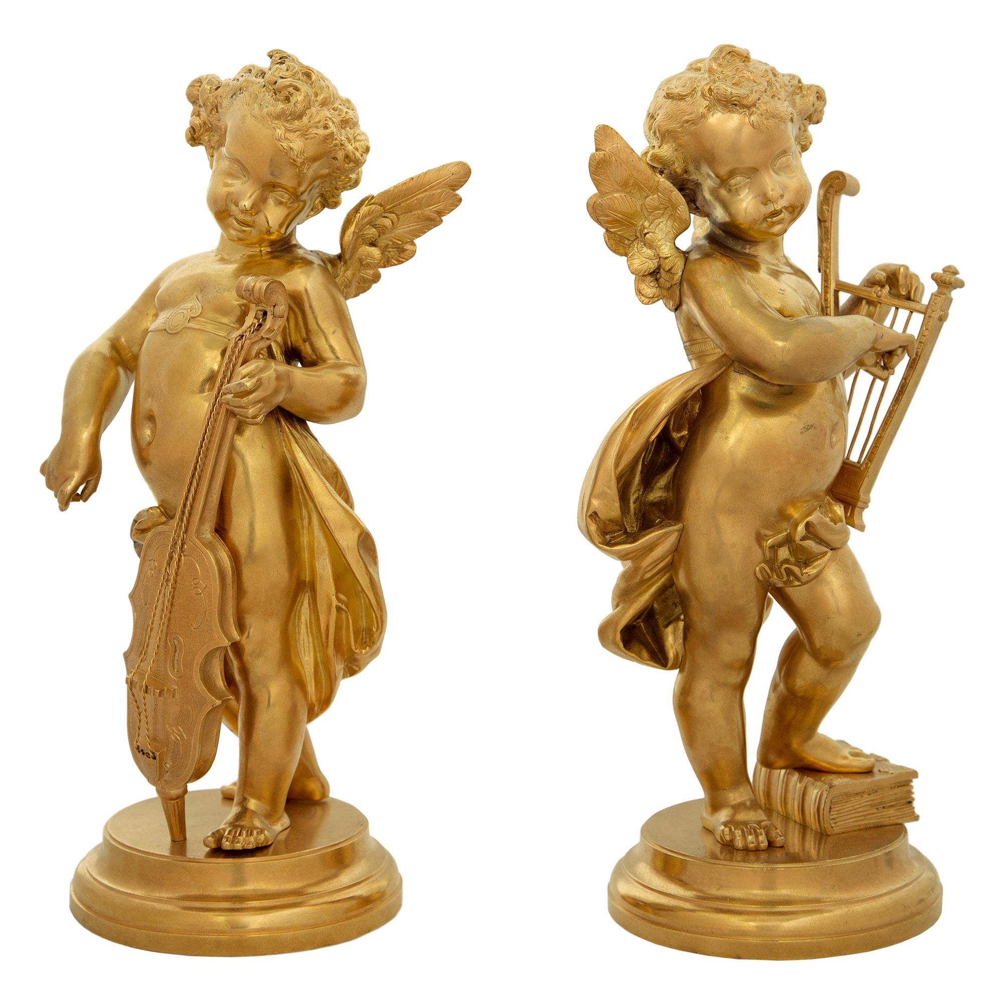 A very charming true pair of French 19th century Louis XVI style ormolu cherub statues. Each richly chased winged cherub displays a joyful expression and stands upon a tapered circular base. One stands upon an ormolu book while playing a delicate