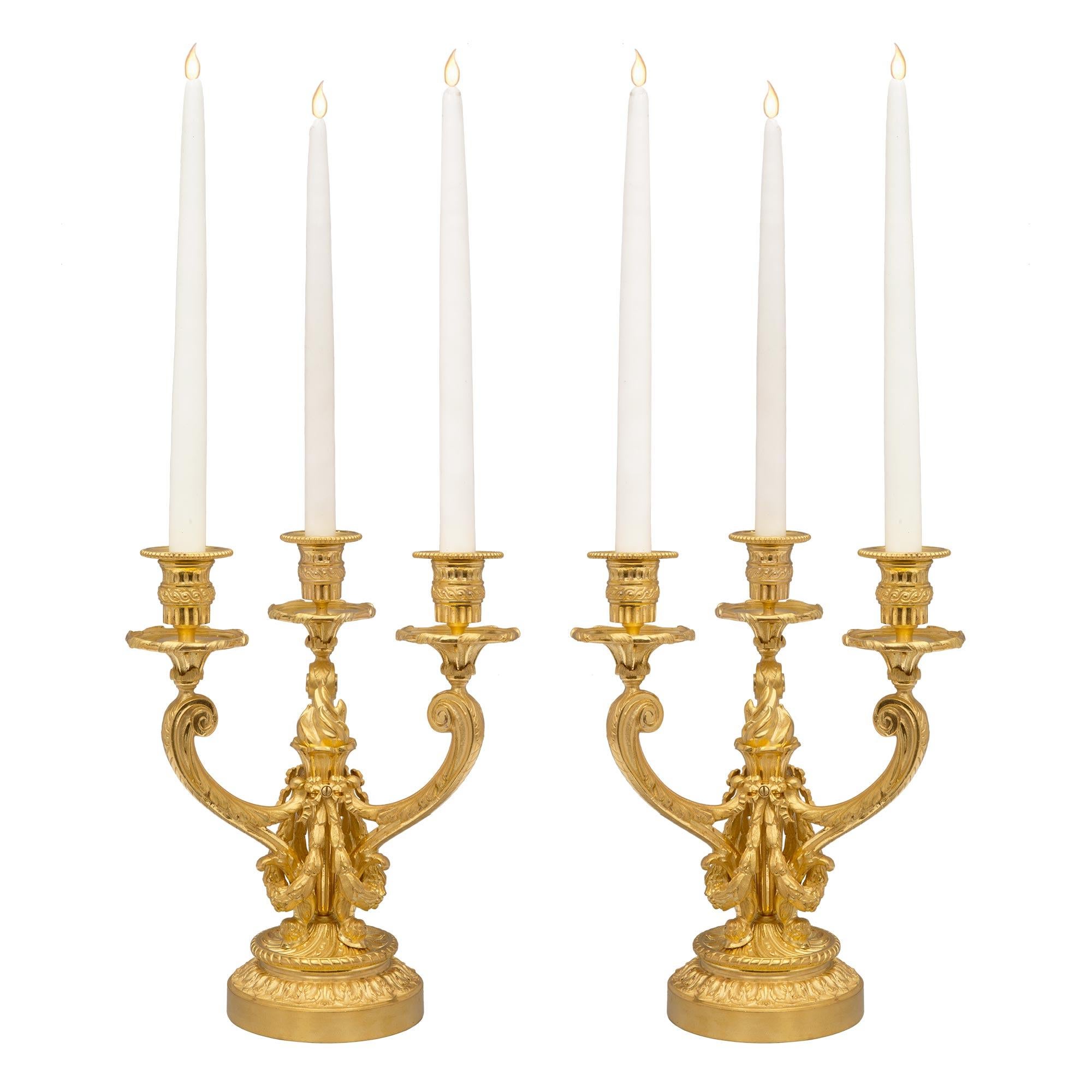 An elegant and high quality pair of French 19th century Louis XVI st. ormolu three arm candelabras. Each candelabra is raised by a circular base with beautiful foliate and a twisted wrap around designs. The three arms branch out form the impressive
