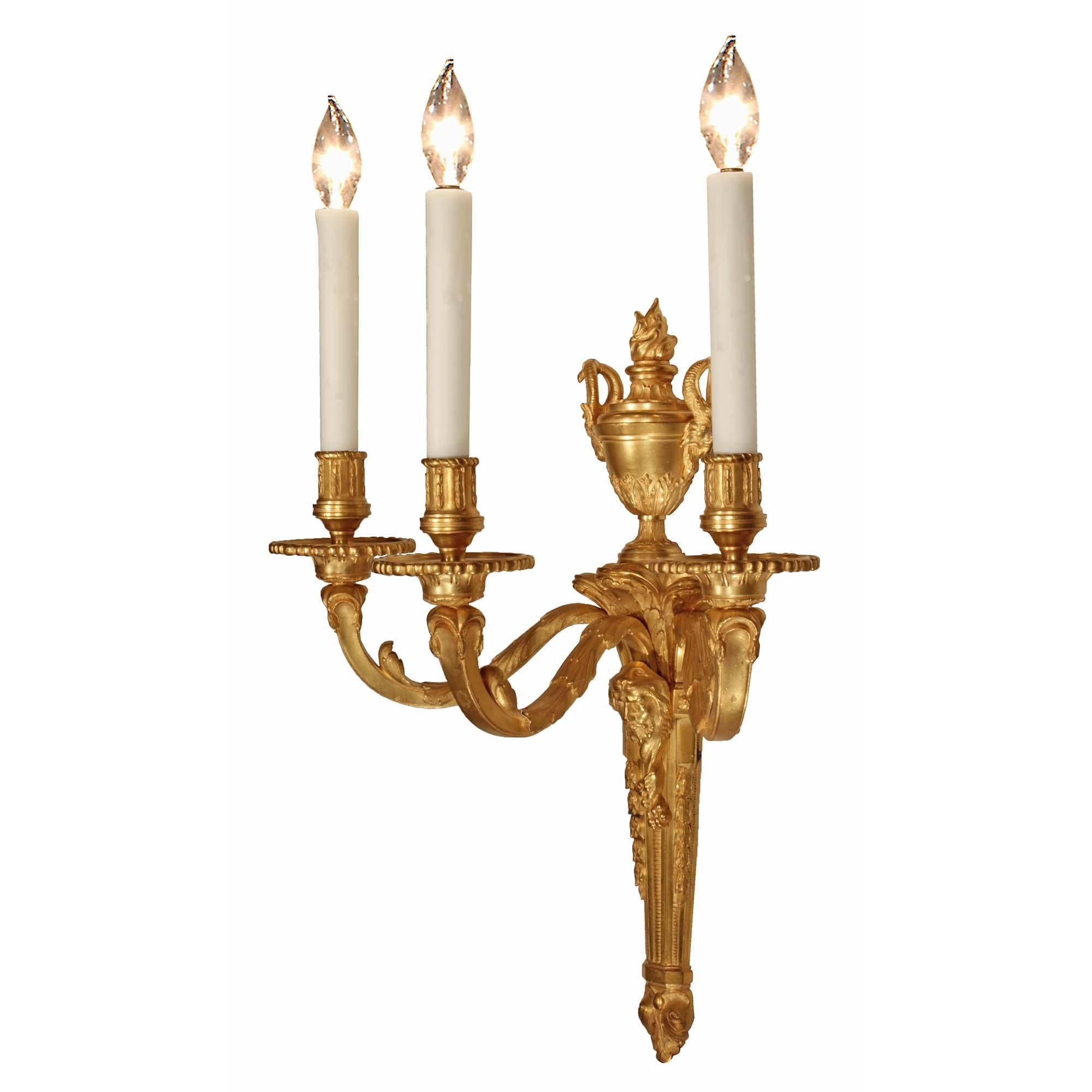 An elegant pair of French 19th century Louis XVI st. ormolu three-arm sconces. Each sconce is centered by a fine bottom acorn finial below the lovely tapering fut with the floral and reeded pattern. At the center is a richly chased Hercules wearing