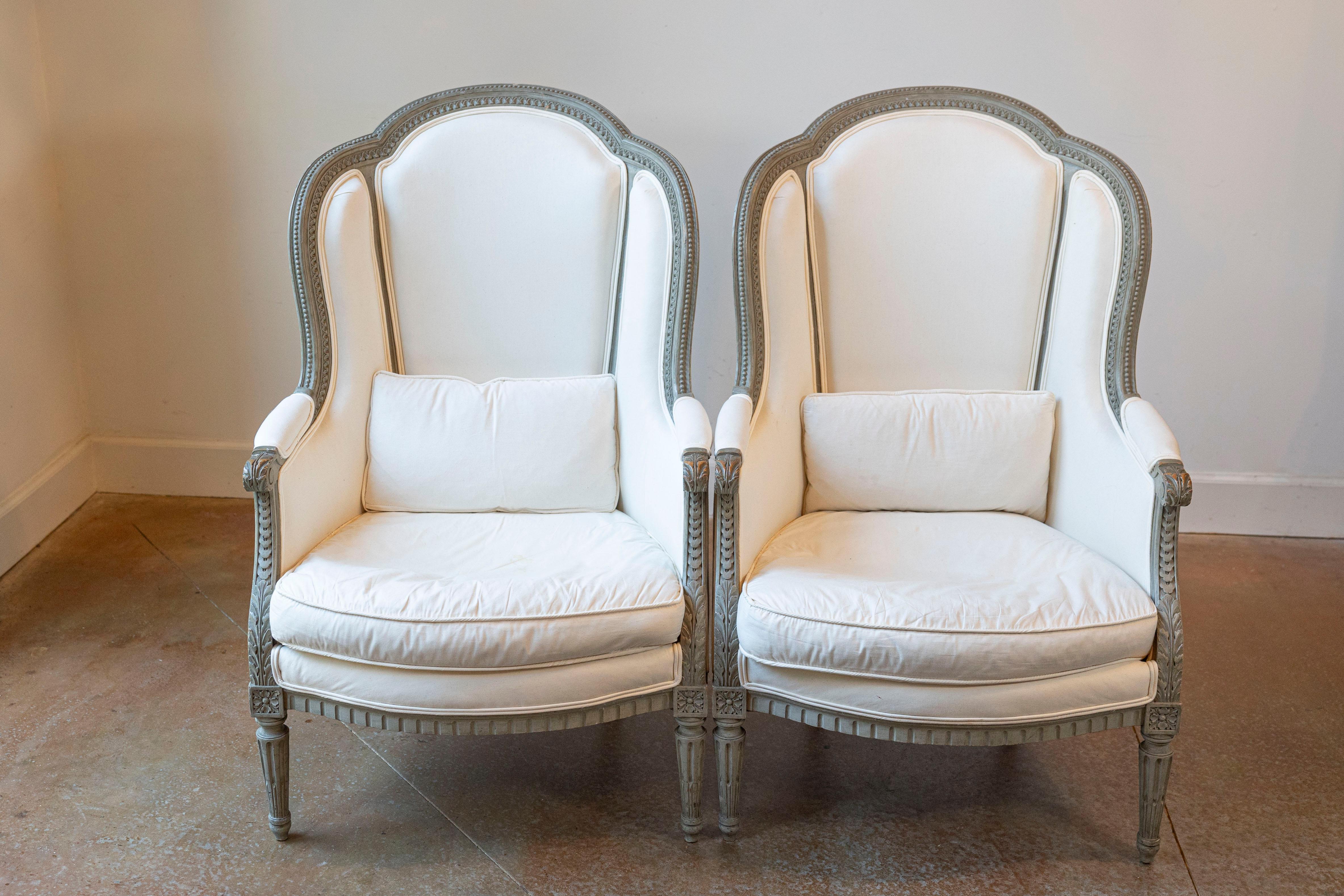 A pair of French Louis XVI style painted wood wingback bergères chairs from the 19th century, with carved décor and new upholstery. Created in France during the 19th century, each of this pair of bergères features a winged back, designed to provide