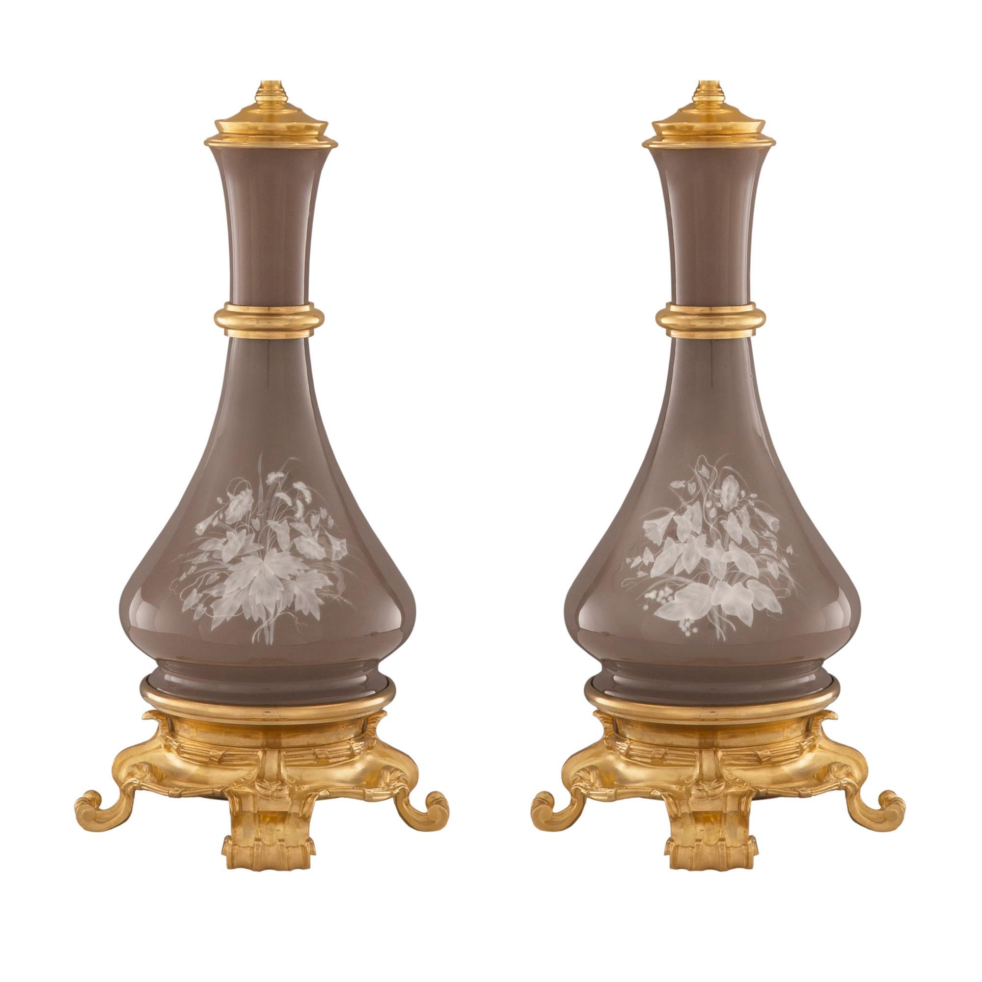 A most elegant pair of French 19th century Louis XVI st. porcelain and ormolu Pâte sur Pâte lamps. Each lamp is raised by a fine ormolu base with most decorative scrolled foliate feet and a lovely hammered design. Above the base are tied fluted