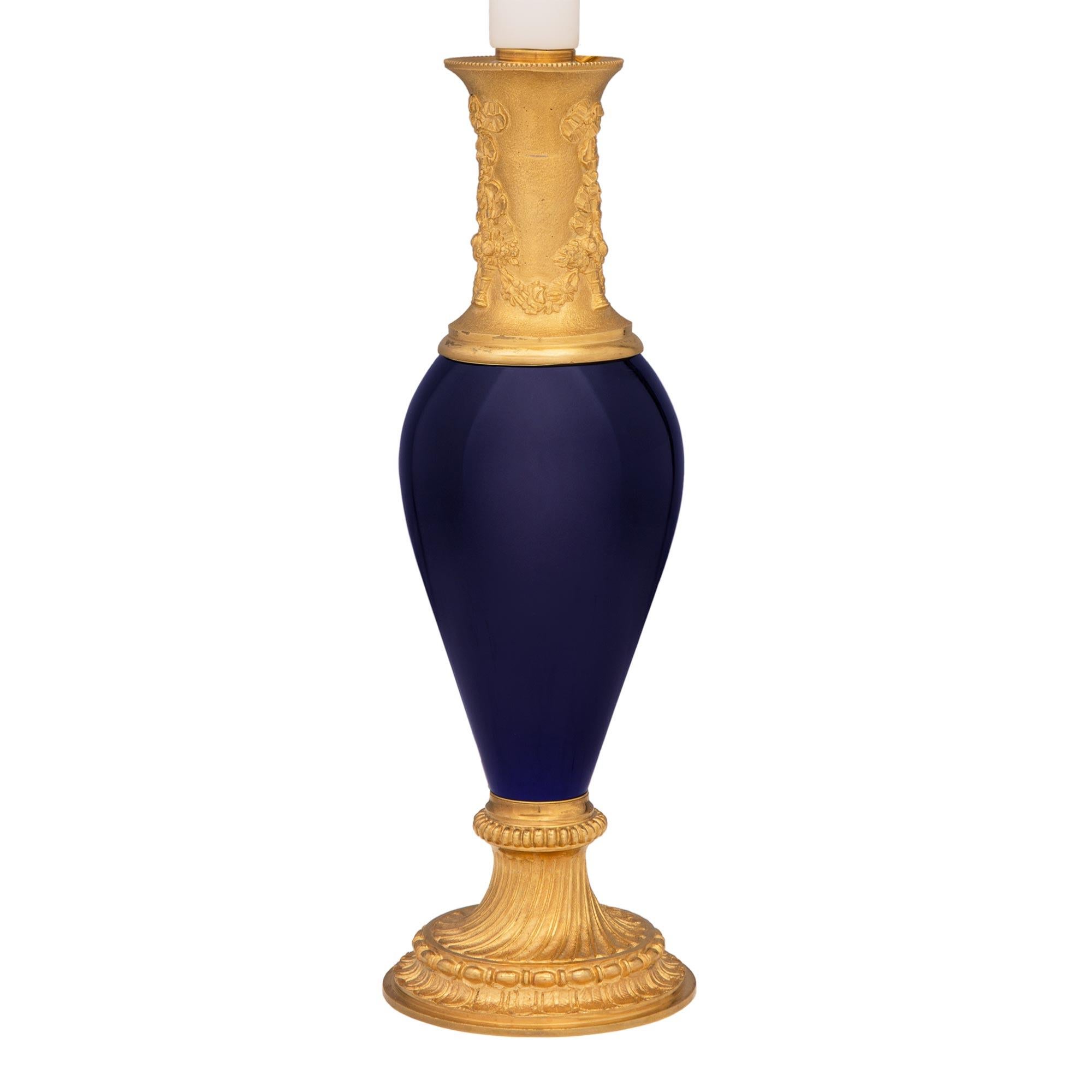 A charming and high quality pair of French 19th century Louis XVI st. cobalt blue porcelain and ormolu lamps. Each small scale lamp is raised by an elegant circular mottled base with lovely foliate designs wrap around beaded bands and beautiful