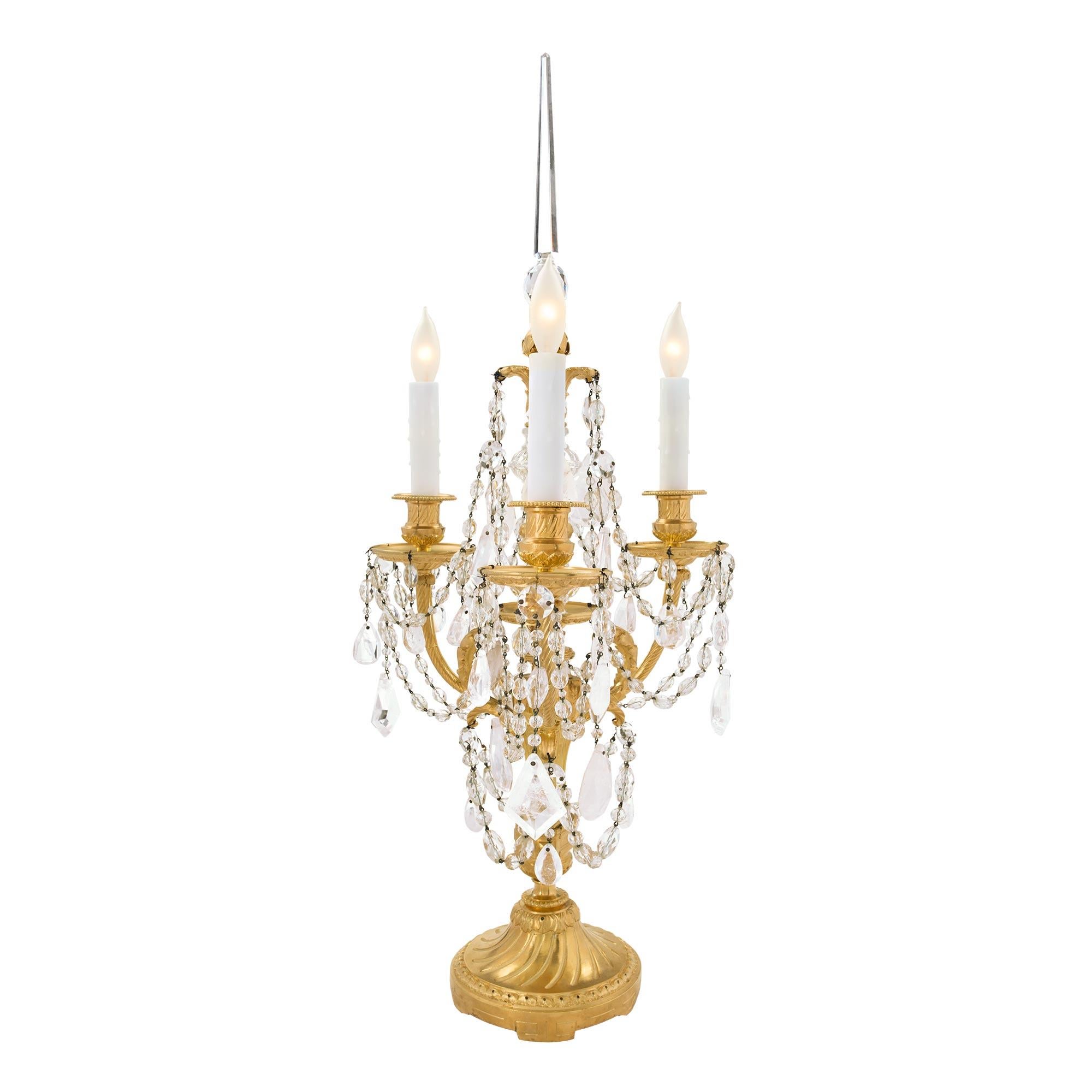 An elegant pair of French 19th century Louis XVI st. ormolu, Baccarat crystal and rock crystal three arm Girandoles lamps. Each lamp is raised by a circular base with a fine wrap around foliate band and a spiral fluted design in a rich satin and