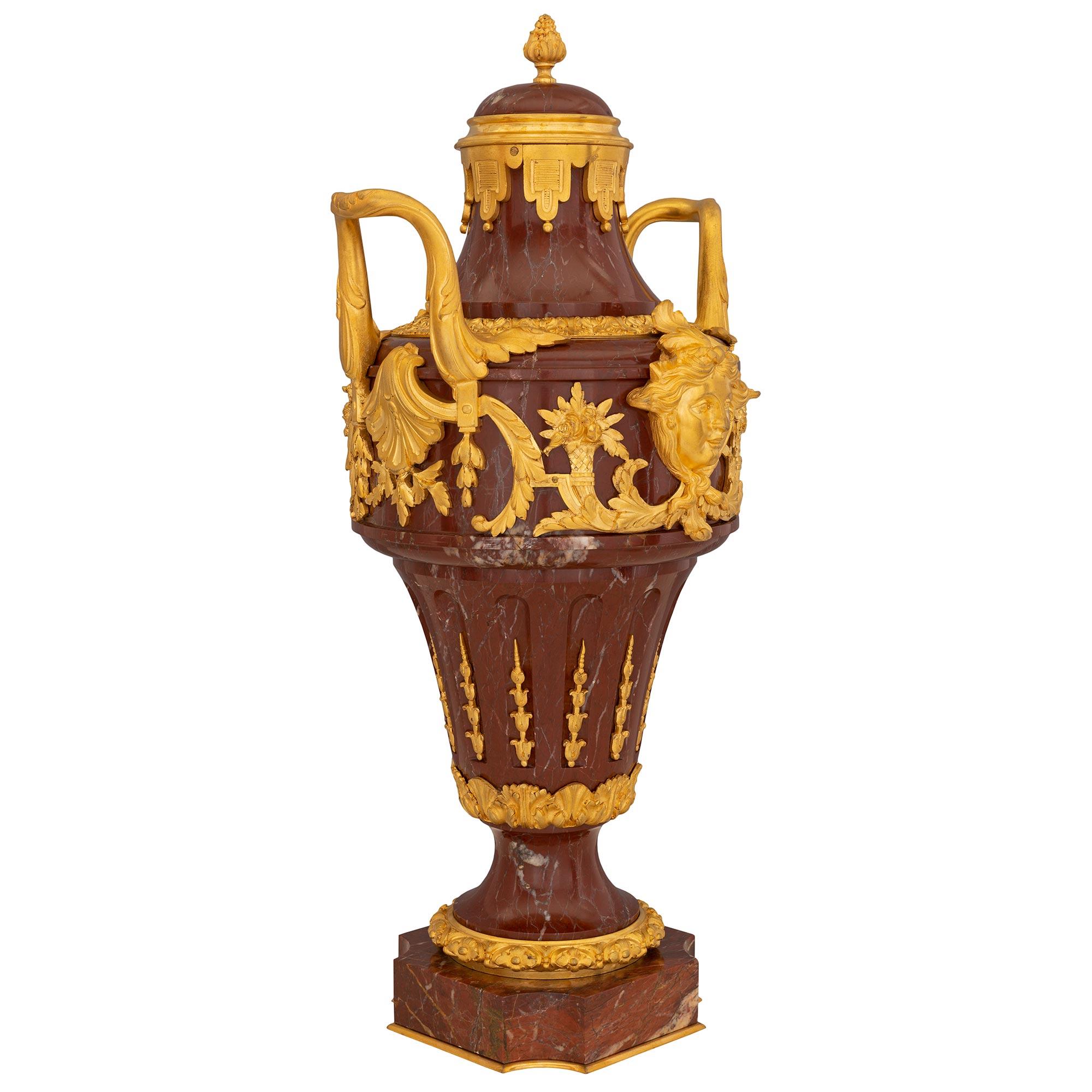 A stunning pair of French 19th century Louis XVI st. Rouge marble and ormolu urns. Each urn is raised by a square base with concave corners and a decorative bottom ormolu fillet. The socle pedestal is decorated with a floral ormolu band and a top