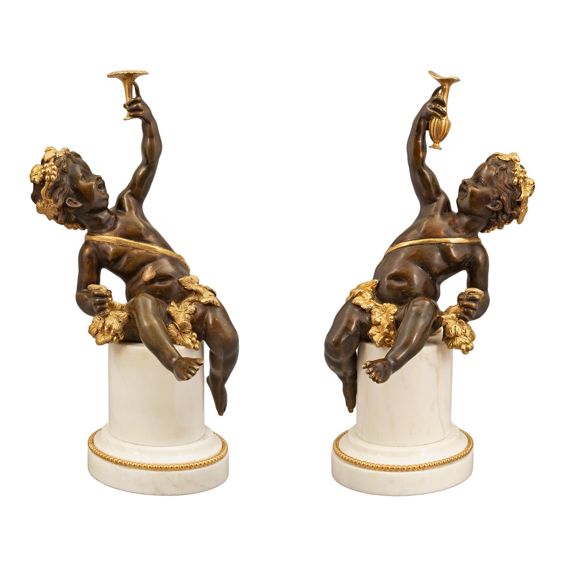 A most charming and high quality true pair of French 19th century Louis XVI st. patinated bronze, ormolu, and white carrara marble statues of joyful cherubs. Each statue is raised by a mottled circular white carrara marble column with a fine ormolu