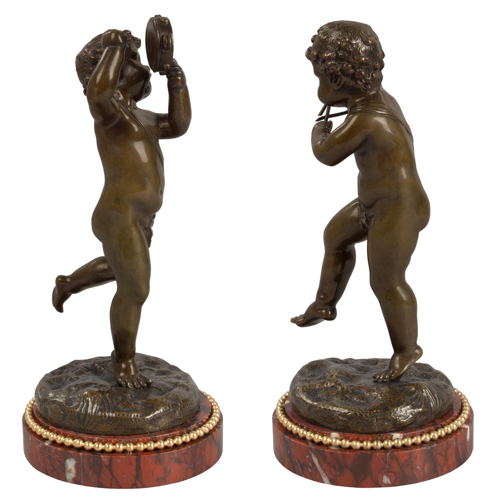 A charming and high quality pair of French 19th century Louis XVI st. patinated bronze, ormolu and rouge Griotte marble statues signed Clodion. Each small statue is raised by a circular rouge Griotte marble base with a mottled border and a finely