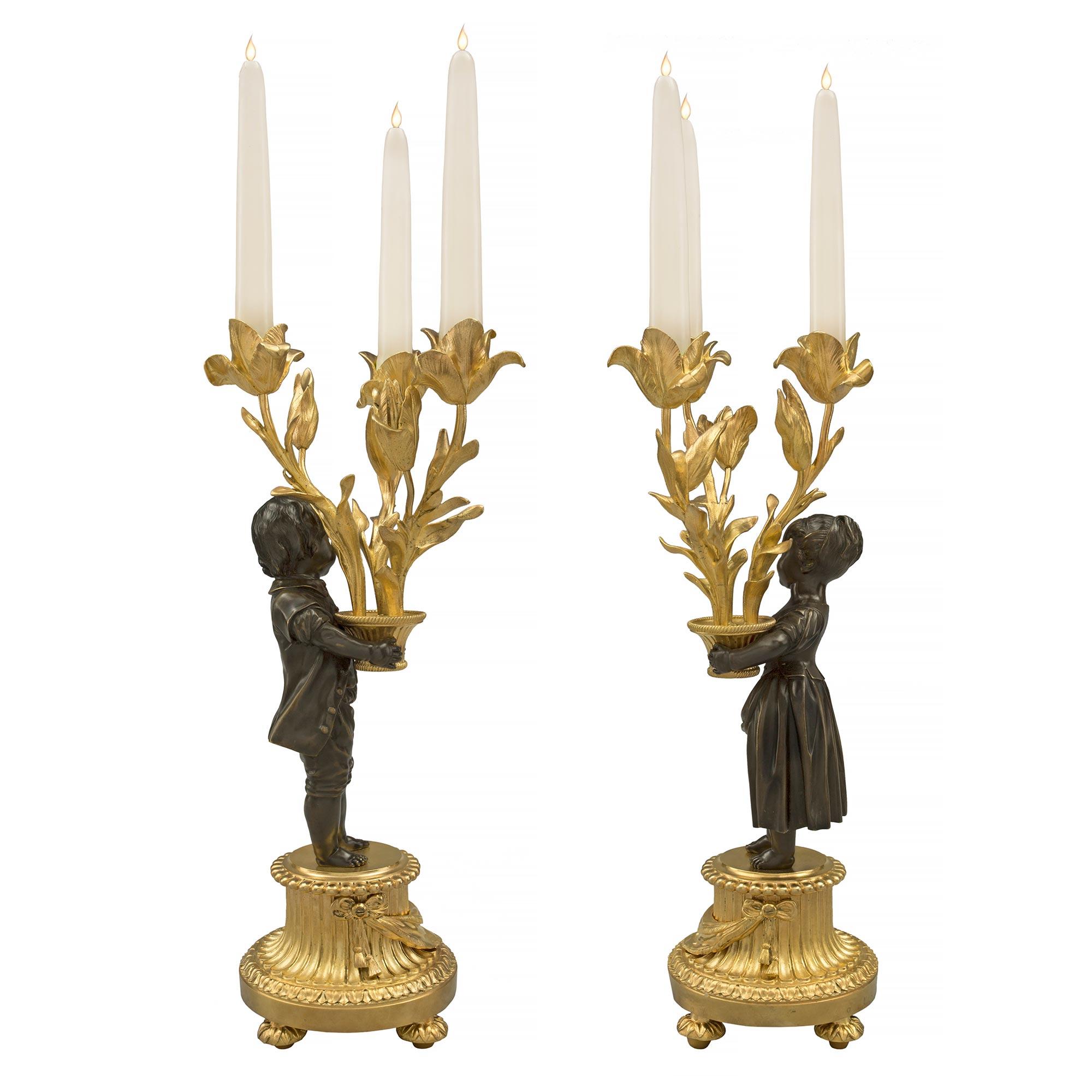 An extremely elegant true pair of French 19th century Louis XVI st. ormolu and patinated bronze three arm candelabras. Each candelabra is raised by four foliate topie shaped feet below the reeded mottled circular base decorated with a finely chased