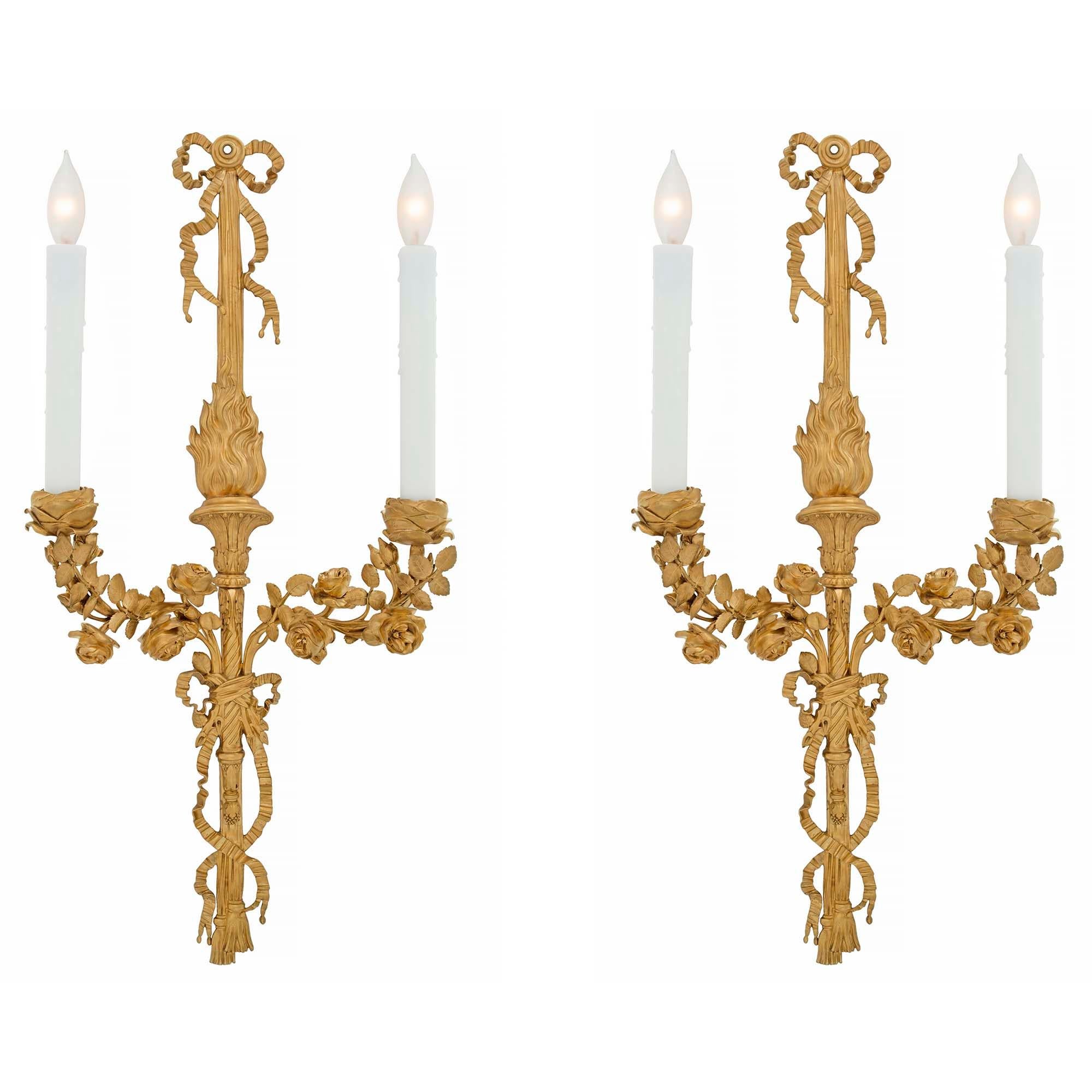 An elegant and high quality pair of French 19th century Louis XVI style two arm ormolu sconces. Each scone is centered by fine tassels below a tied ribbon design and acorn finial. The arms display impressive and richly chased detailed etched flowers