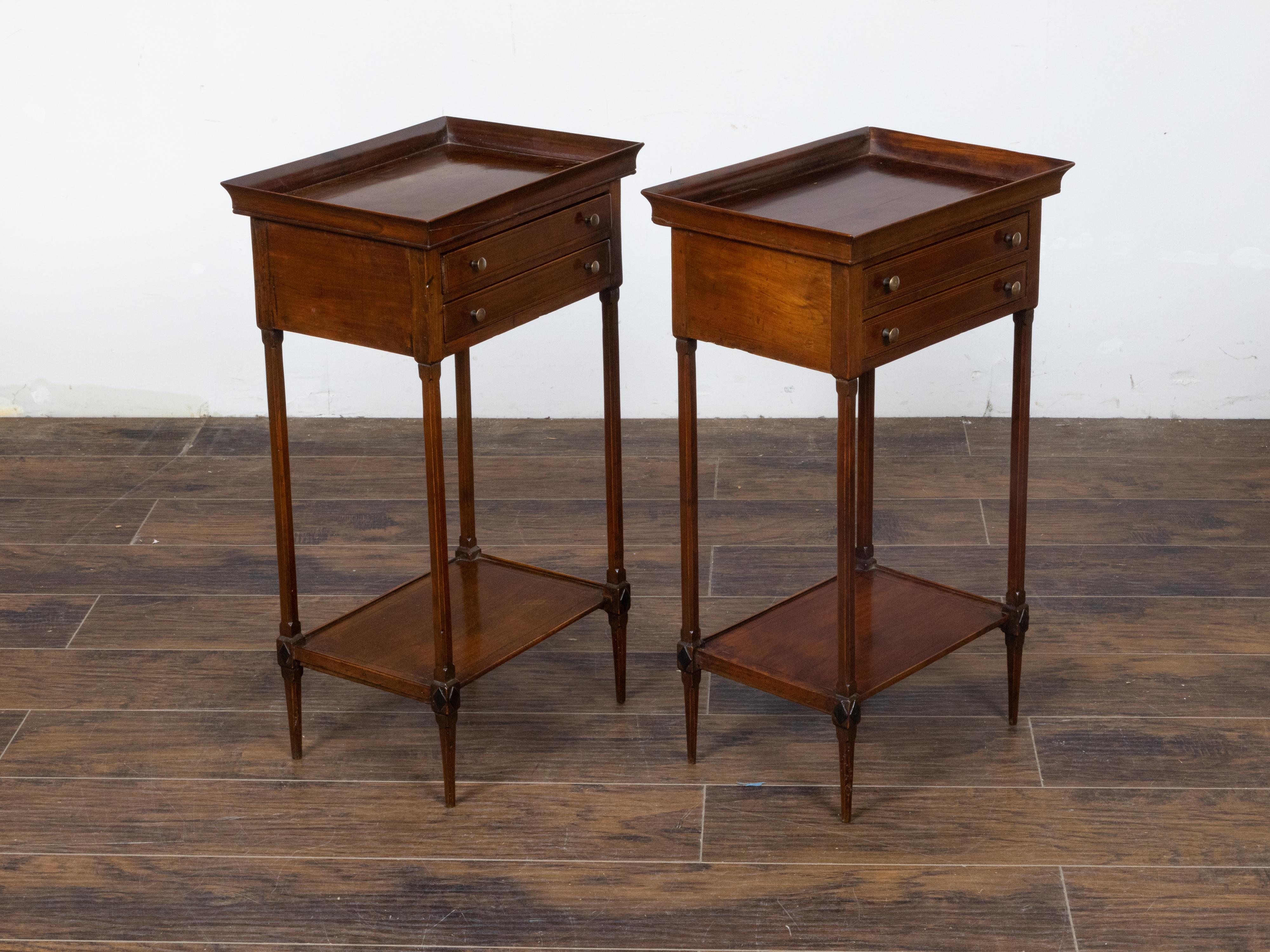 A pair of French mahogany bedside tables from the 19th century with tray tops, two drawers each, discreet banding, lower shelves and ebonized carved diamond motifs on the knees. This elegant pair of French mahogany bedside tables hails from the 19th