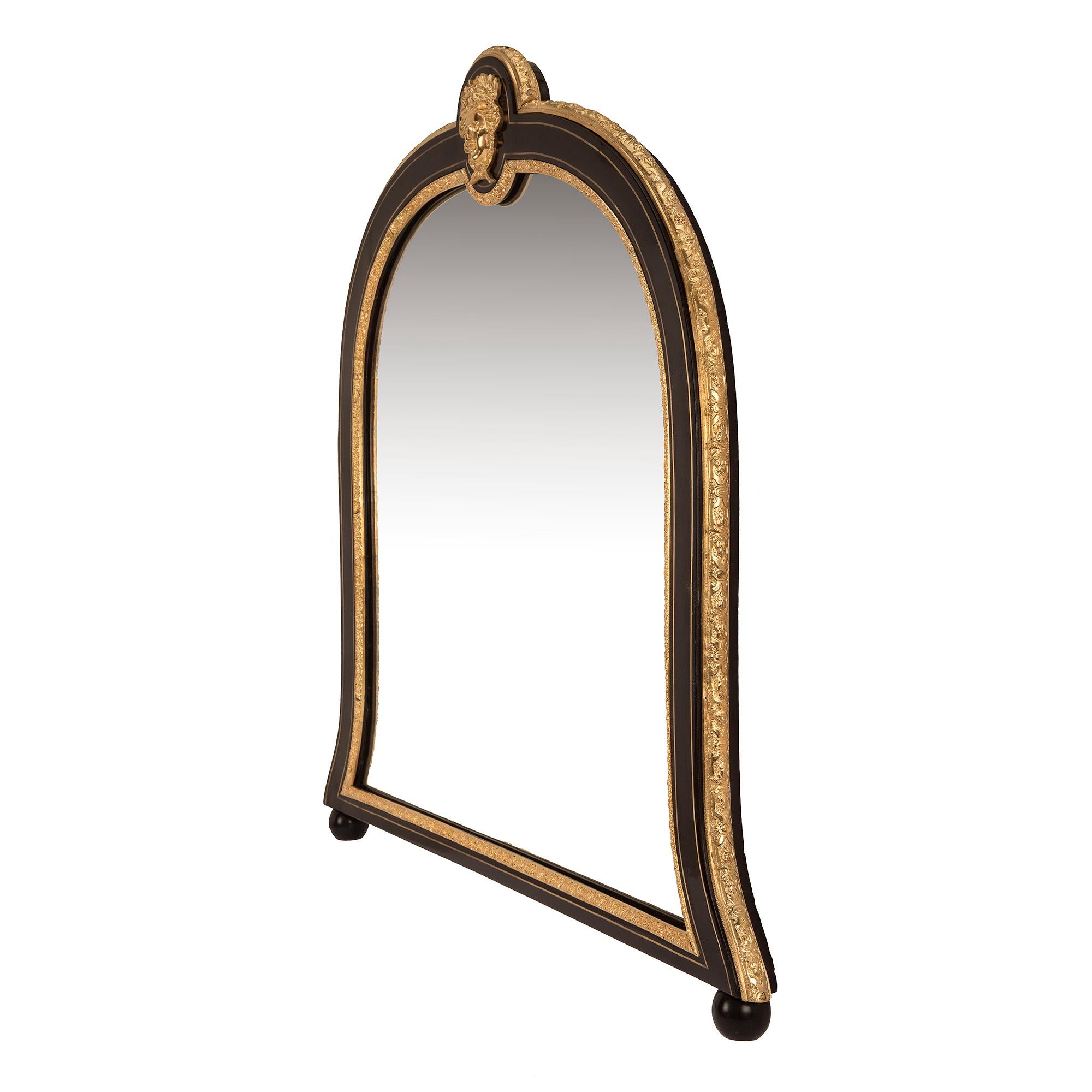 Une paire merveilleuse et très unique de miroirs montés en ébène, laiton et bronze doré, d'époque Napoléon III et de style Louis XIV, datant du 19e siècle. Les miroirs sont surélevés par deux pieds en forme de chignon tandis que les plaques de