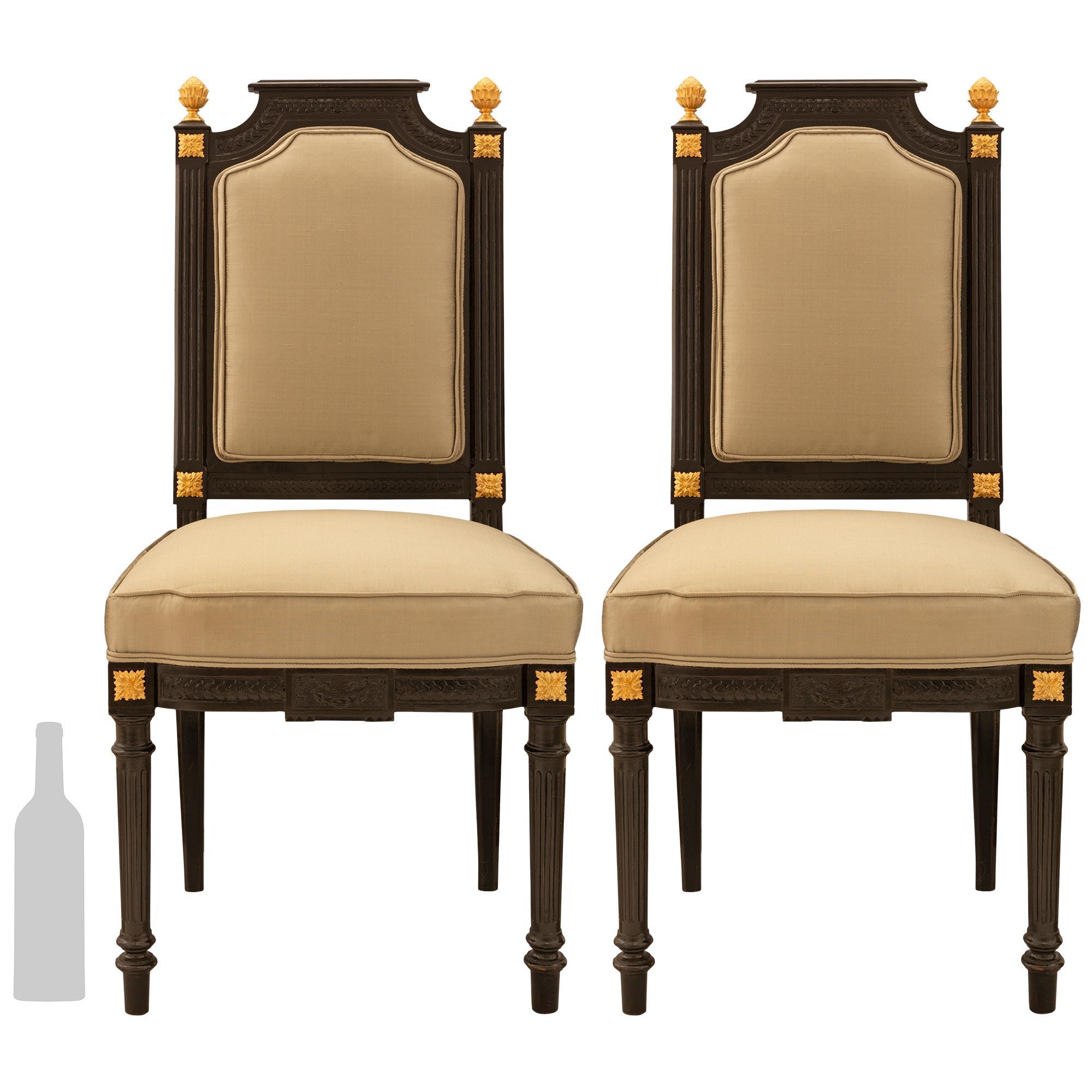 A striking and handsome pair of French 19th century Napoleon III period Louis XVI st. ebony and ormolu side chairs with unusually wide seats. Each chair is raised on four circular tapered fluted legs below richly chased ormolu recessed block