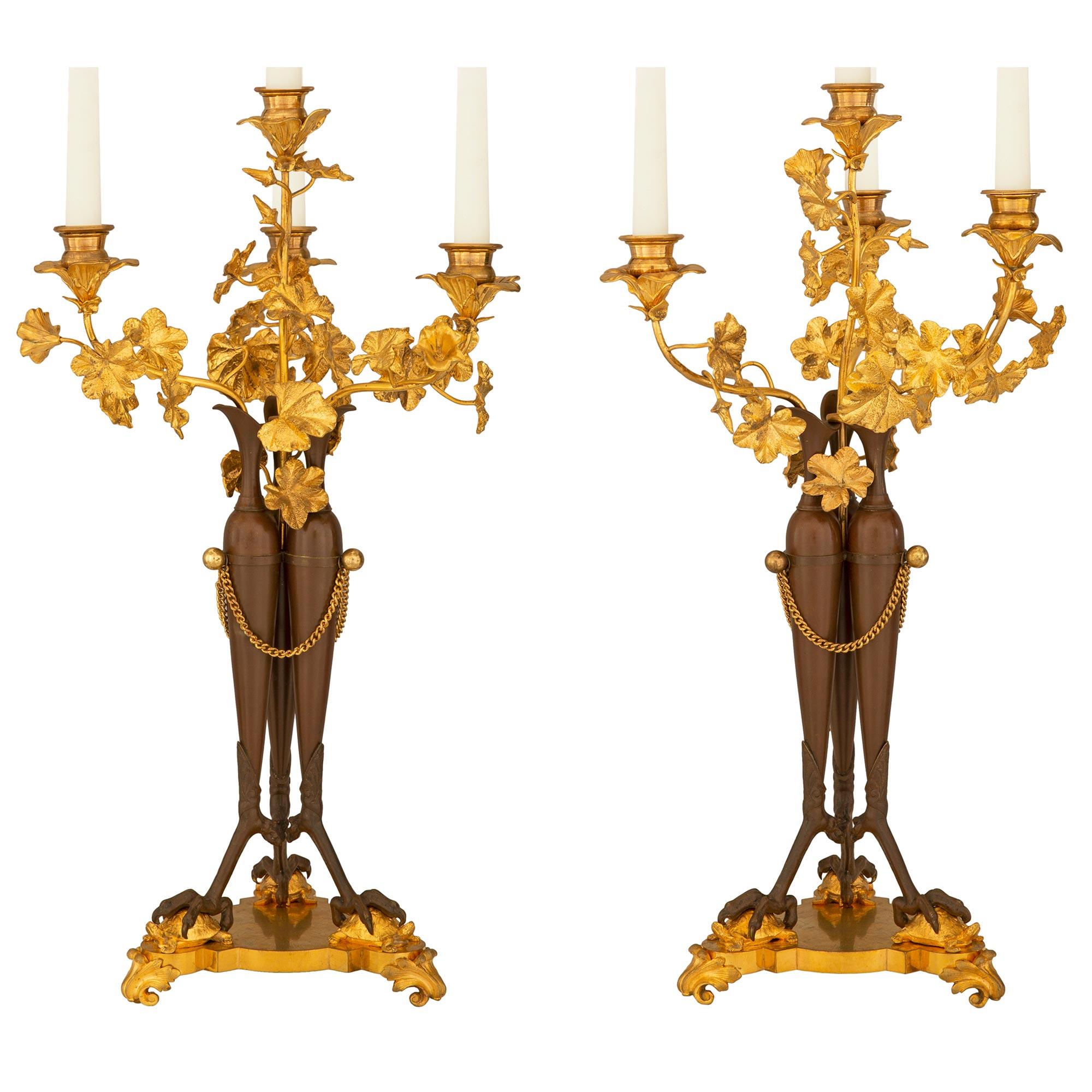 A striking pair of French 19th century neoclassical st. patinated bronze and ormolu candelabras. Each four arm candelabra is raised by a triangular scalloped base with fine scrolled foliate feet below impressive claws holding charming finely
