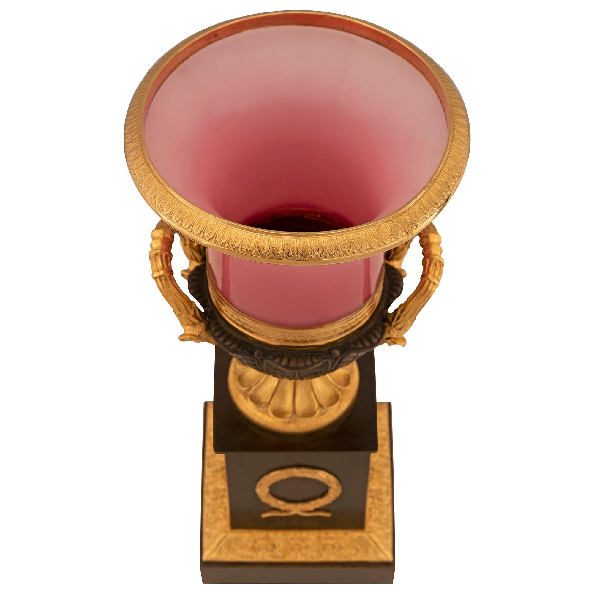 Une paire d'urnes néoclassiques du XIXe siècle en bronze patiné, bronze doré et verre. Chaque urne est surmontée d'une base carrée ornée d'une fine bande de bronze doré tachetée et d'une élégante couronne de laurier à baies au centre du support.
