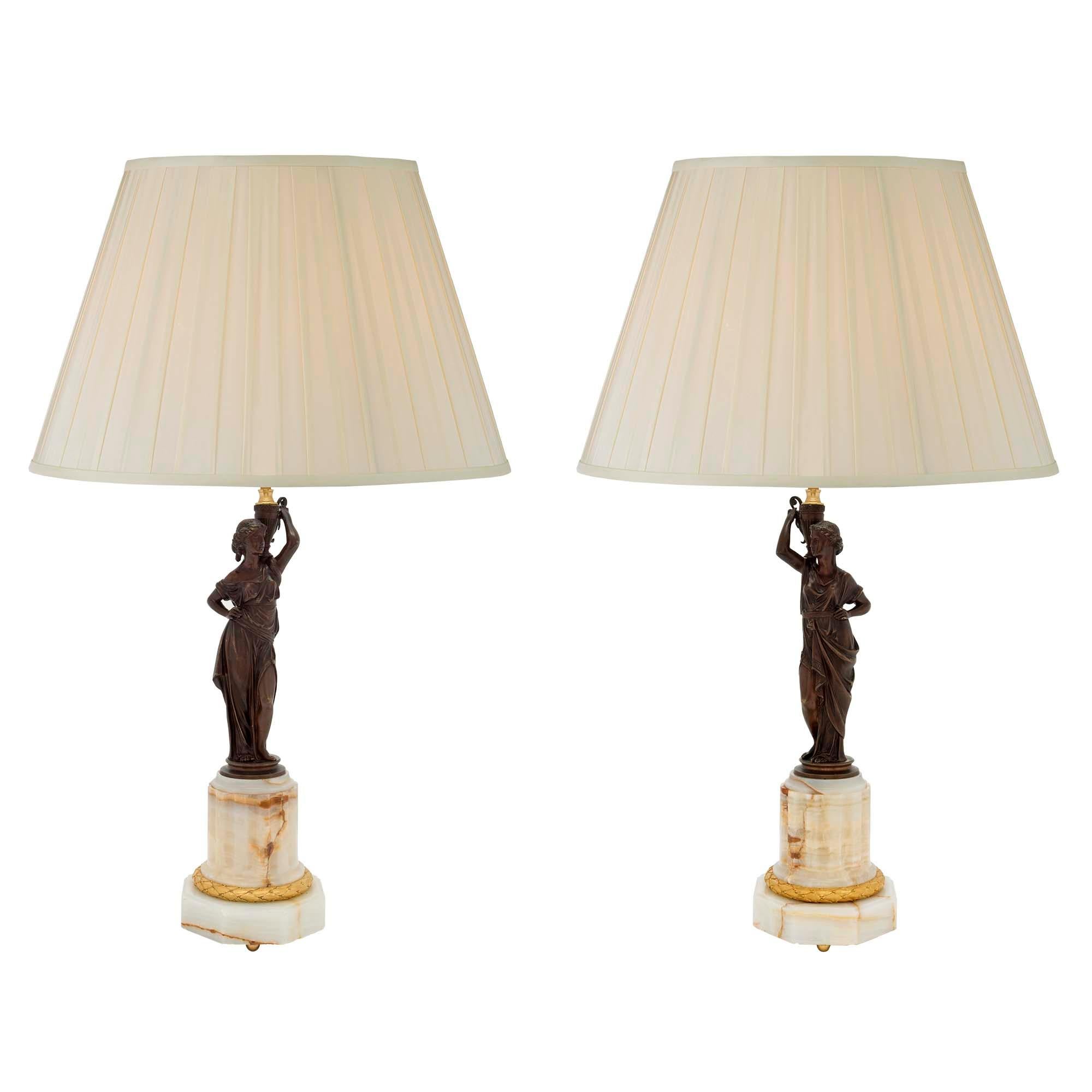 Une paire extrêmement élégante de lampes néoclassiques françaises du 19ème siècle en onyx, bronze doré et bronze patiné. Chaque lampe est surélevée par une base octogonale en onyx avec des pieds à boule en bronze doré, sous un bandeau en bronze doré