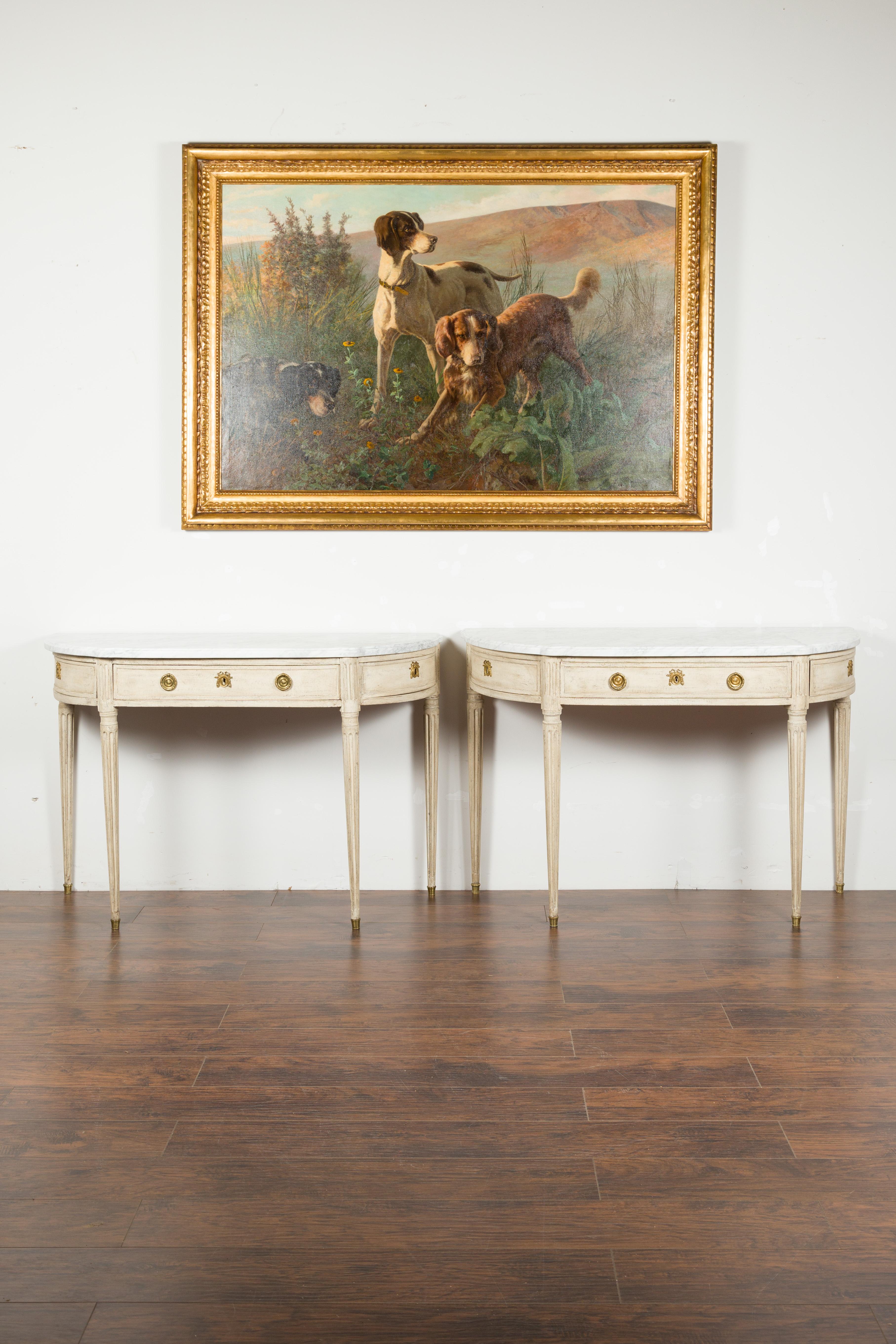 A pair of French neoclassical style painted wood demilune console tables from the 19th century, with white marble tops and fluted accents. Created in France during the 19th century, each of this pair of demilunes features a semi-circular whited