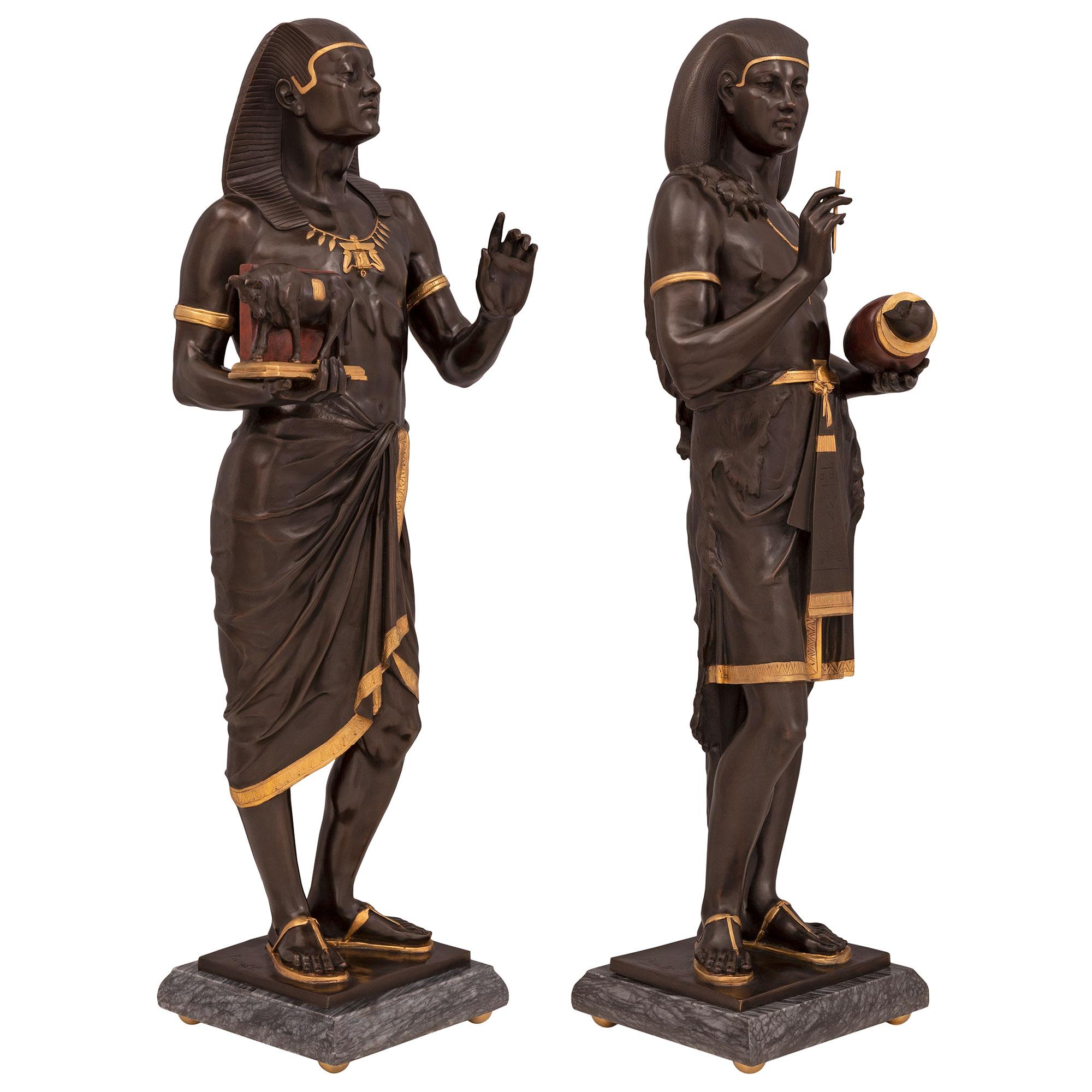 Une paire de statues néo-classiques de style néo-égyptien du 19ème siècle, de très grande qualité et très impressionnante. Néo-égyptien du XIXe siècle, en bronze patiné, bronze doré et marbre, signée PICAULT. Chaque statue est surélevée par une base