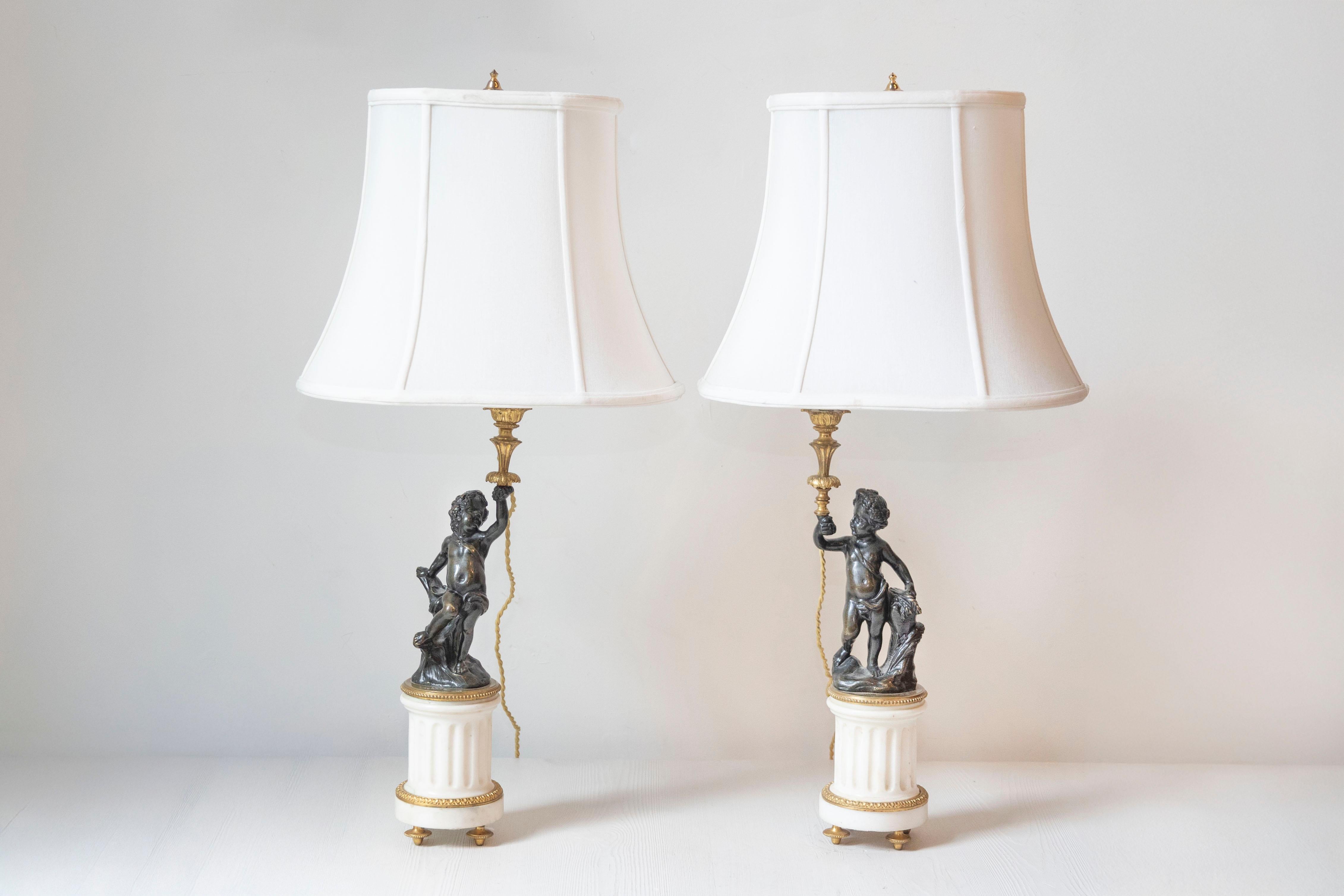 Coppia di lampade a putti in marmo bianco e bronzo in stile neoclassico francese del XIX secolo, con paralume. Creata in Francia durante il XIX secolo, questa coppia di lampade da tavolo attira la nostra attenzione con il suo arredamento neoclassico