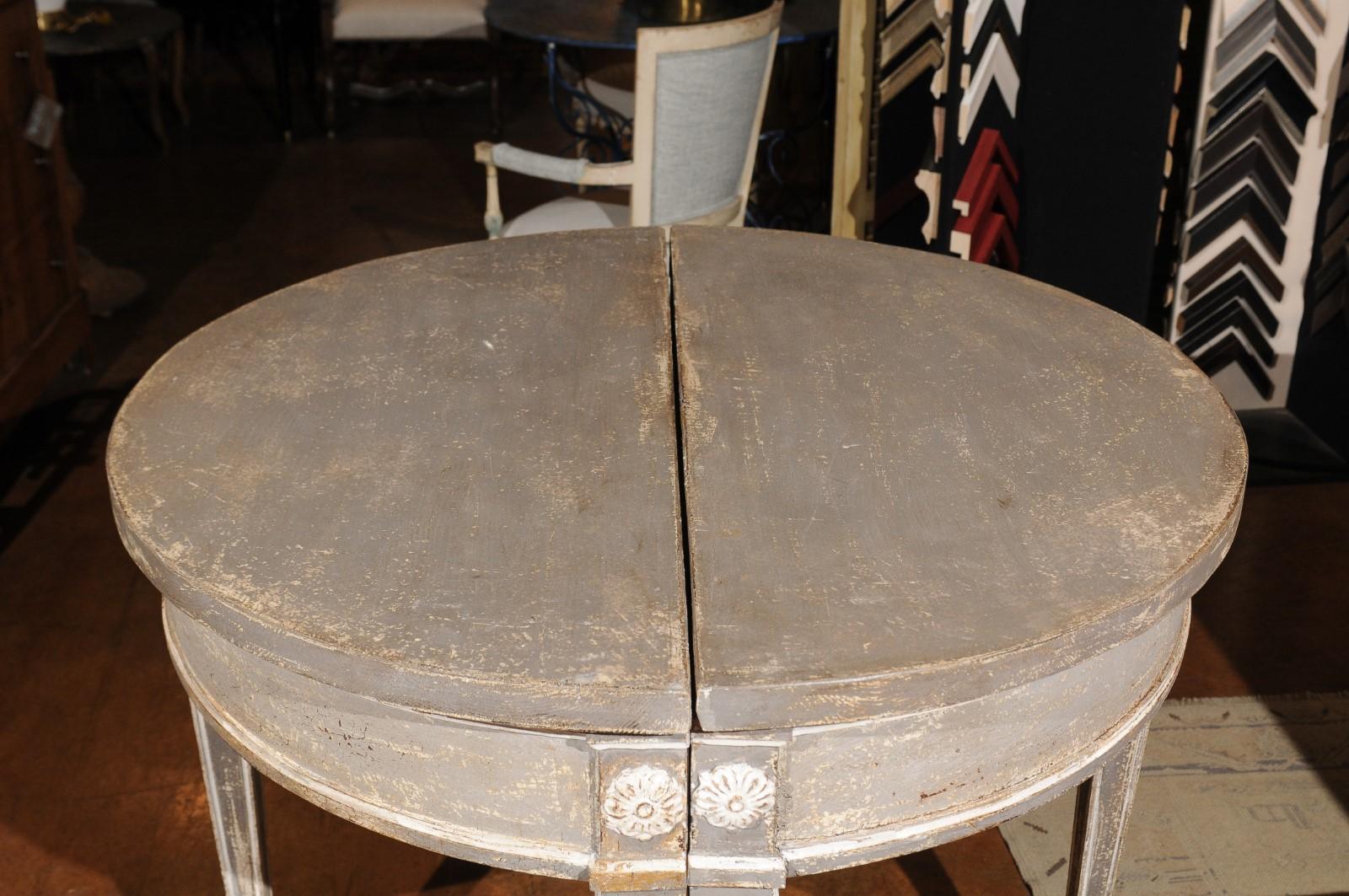 A pair of French neoclassical style painted wood demilune tables from the 19th century, with carved rosettes and tapered legs. Born in France during the politically dynamic 19th century, each of this pair of Neoclassical style demilunes features a