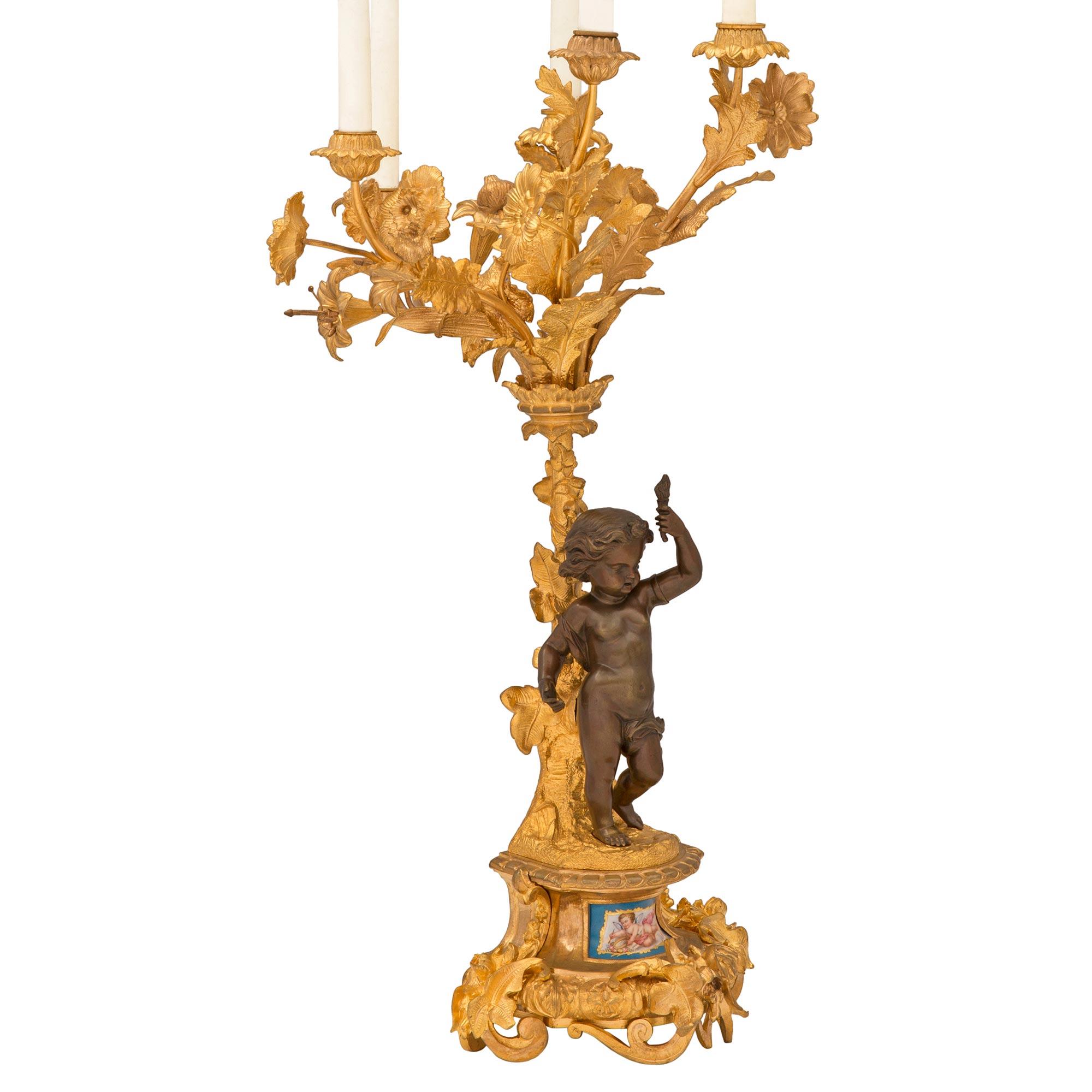A striking true pair of French 19th century Louis XVI st. ormolu, patinated bronze and Sèvres porcelain candelabras. Each five arm candelabra is raised by a stunning pierced scrolled foliate base with lovely floral accents and a beautiful and most