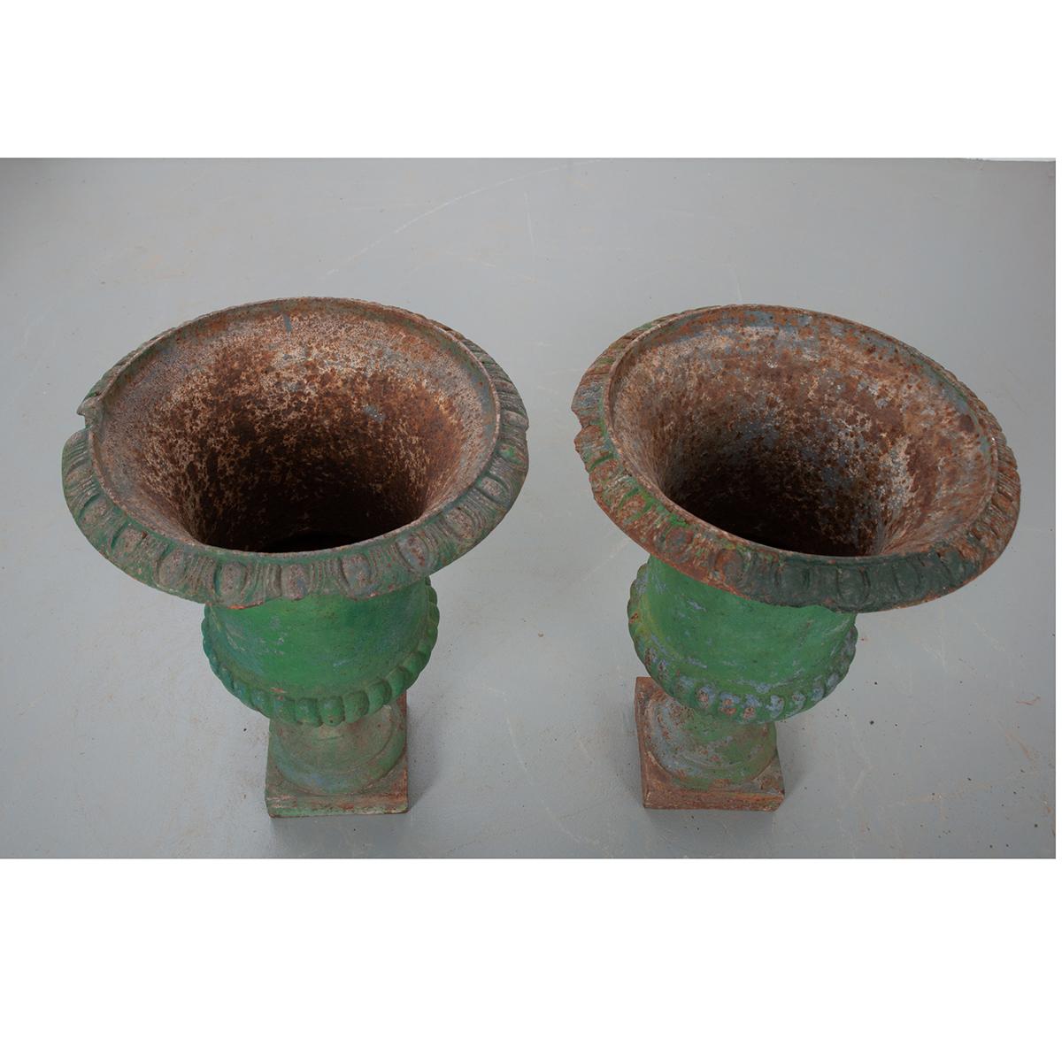 A fantastic pair of classical cast iron pots from 19th century France. These pots have multiple layers of paint with different colors showing through its incredible, aged patina. Both urns are equipped with a drain and could be used both indoors and