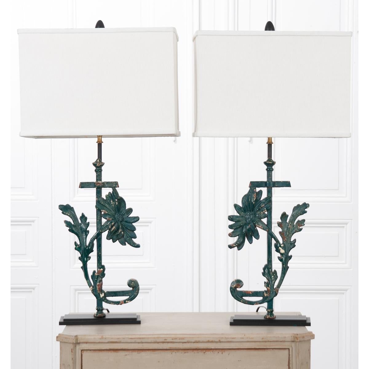 A beautiful pair of custom lamps made from decorative painted iron segments that have been mounted to a base and rod to create an extraordinary pair of lighting fixtures. The lamps are mirror images of a flower and leaf motif in a dark green color