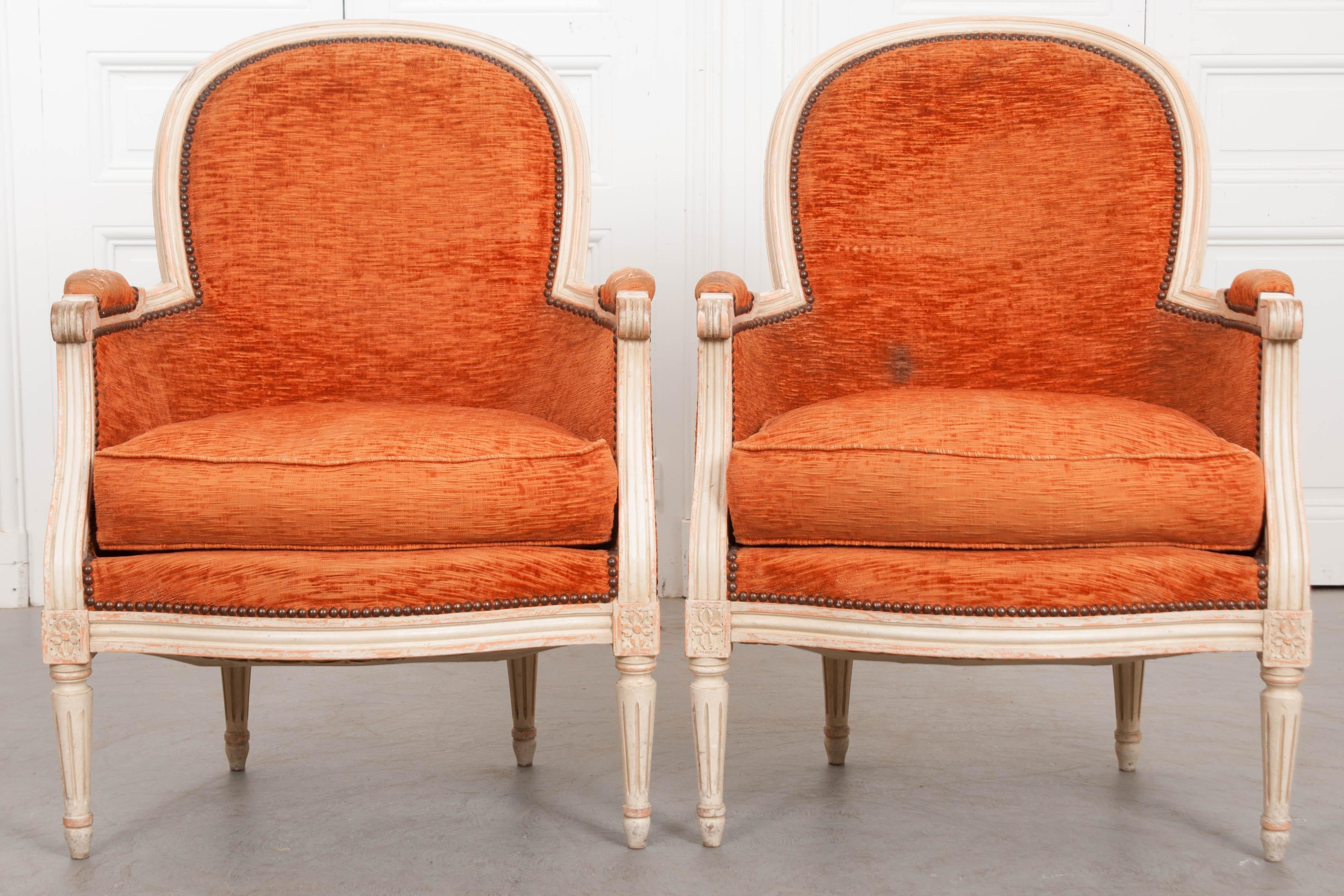 A pair of painted and upholstered French 19th century Louis XVI style bergères. The chairs date to the 1870s, when they would have been carved and painted by hand. The frames still wear their original paint, which has become beautifully worn over