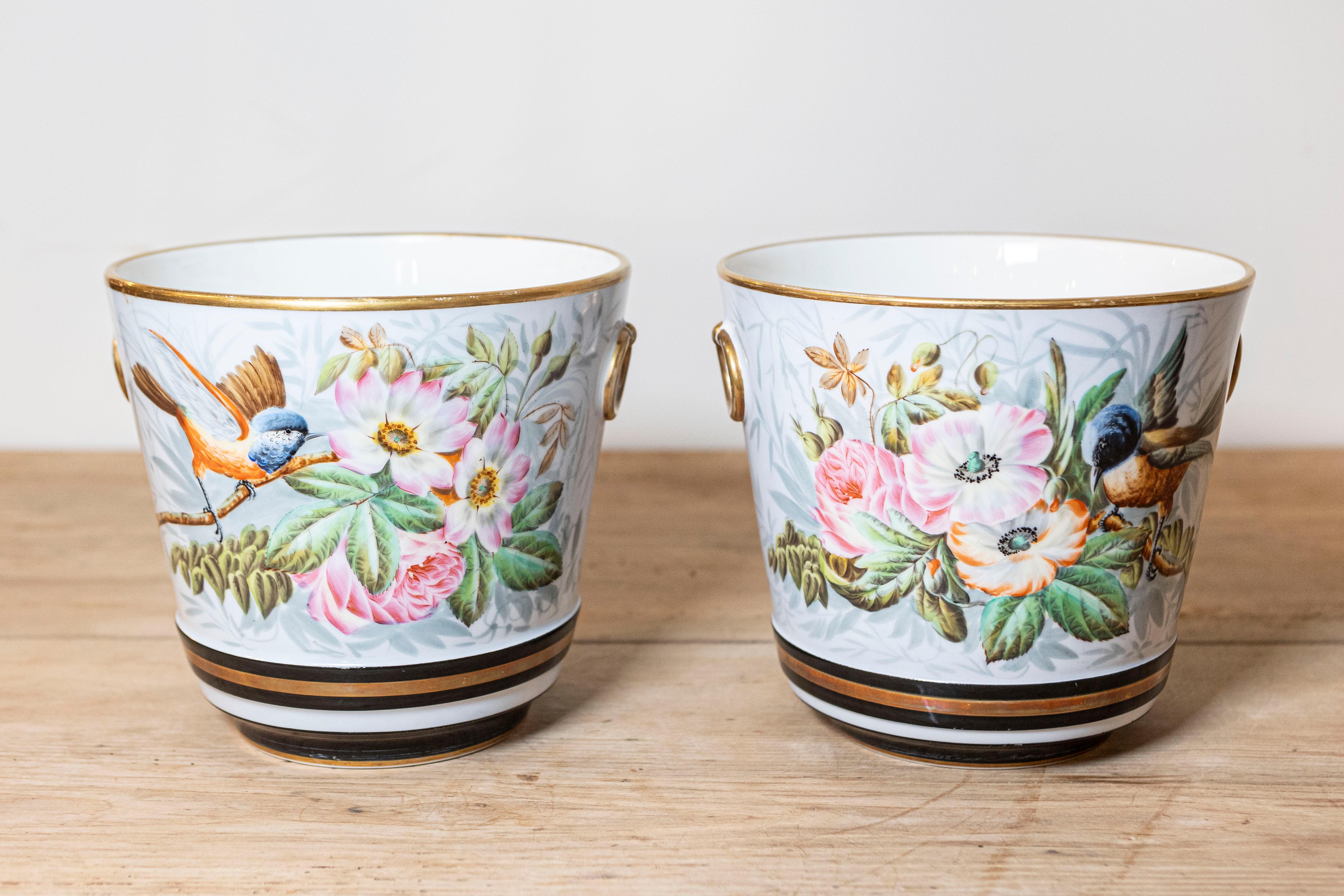 Coppia di vasi da fiori in Porcelaine de Paris del XIX secolo, con motivi floreali e uccelli dipinti a mano e accenti dorati. Creata in Francia nel XIX secolo, questa coppia di cachepot presenta un corpo circolare affusolato, ornato da un delicato