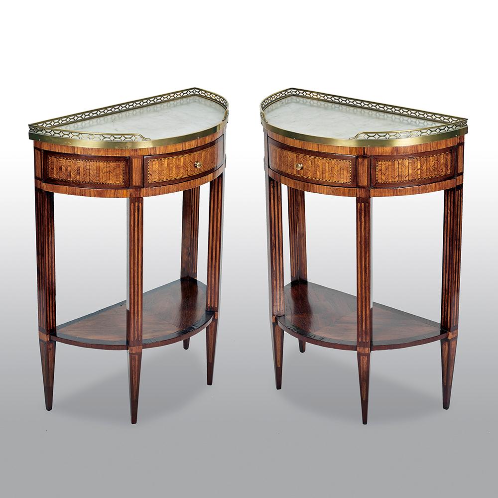 A pair of French kingwood, tulipwood and parquetry demilune side tables, with white marble tops within a raised brass gallery. Below the parquetry frieze drawer, four slender graduating legs supporting a lower tier.