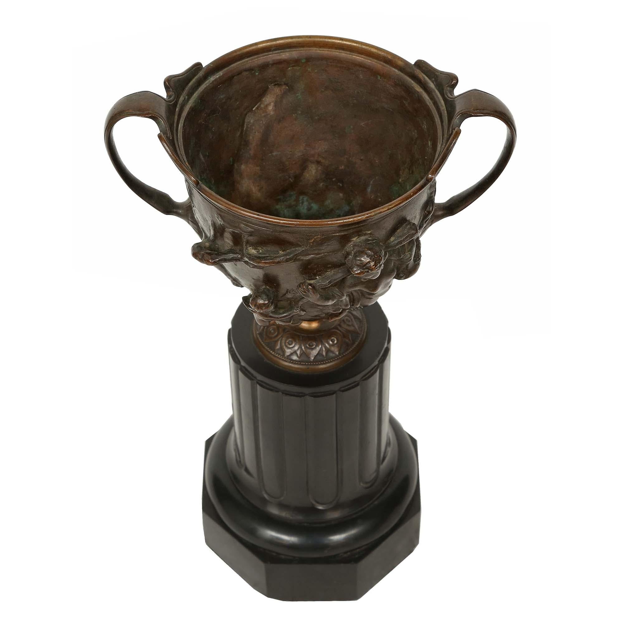 Una coppia molto attraente di tazze francesi in bronzo patinato del XIX secolo, sollevate da una base in marmo nero belga con colonna alta e a forma di zoccolo ottagonale. Sopra la base c'è un supporto circolare con un disegno di foglie d'acqua. Le