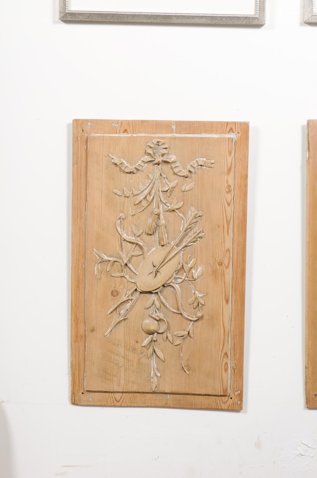 A pair of French pine panels from the 19th century, depicting hand-carved ribbon-tied arrow-pierced tambourines and castanets. Created in France during the 19th century, each of this pair of pine panels attracts our attention with its lovely