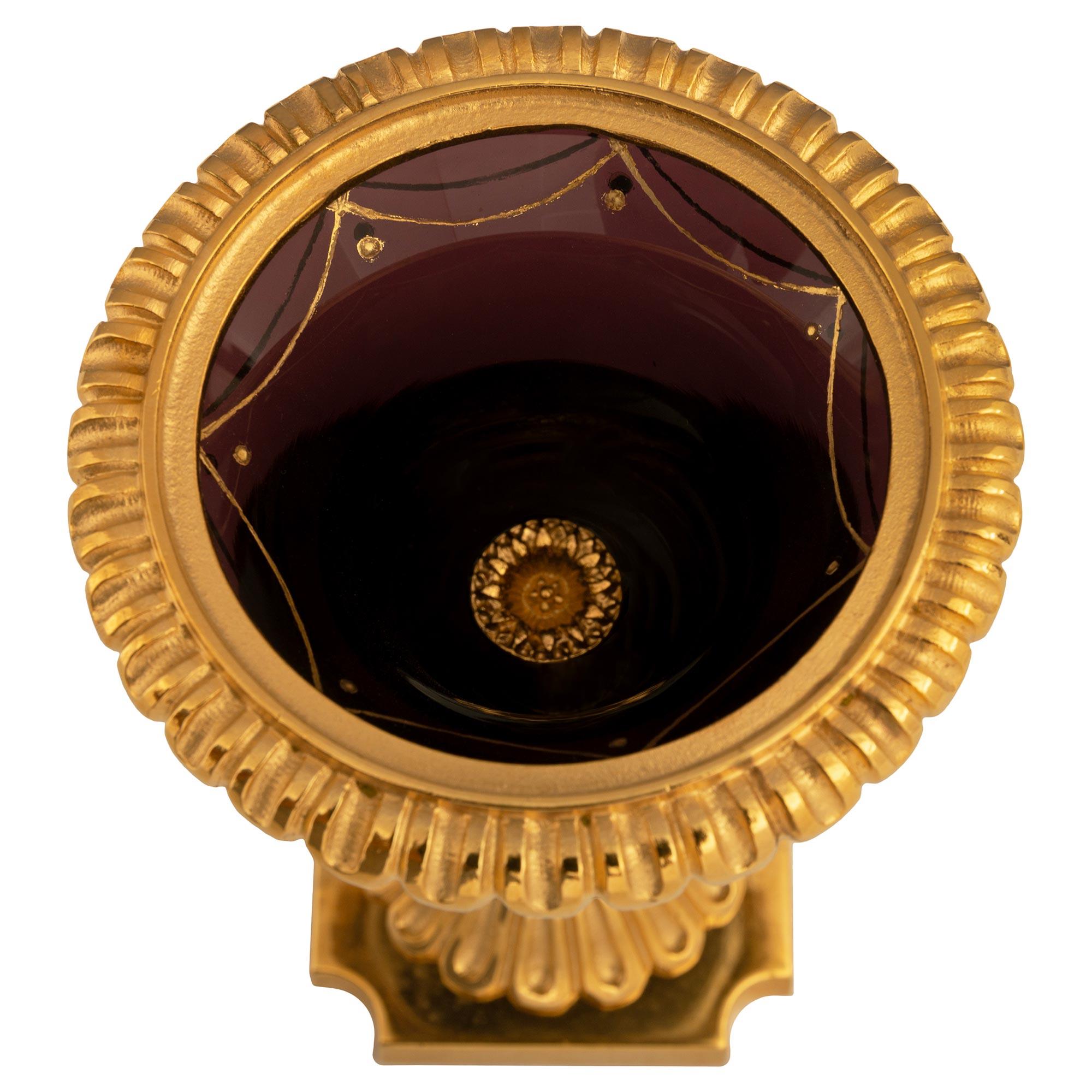 Una coppia molto elegante e di piccole dimensioni di vasi francesi del XIX secolo in vetro viola e Ormolu. La coppia è sollevata su basi quadrate in Ormolu con angoli concavi. Sopra c'è il piedistallo circolare con un disegno scanalato sotto il
