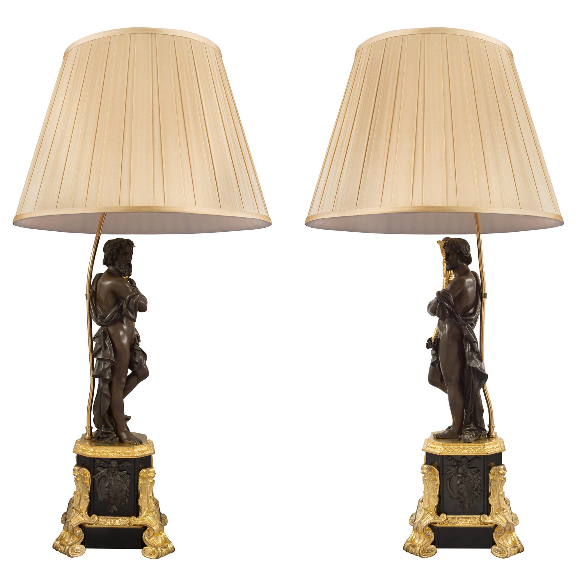 Une paire très impressionnante de lampes françaises de style Renaissance du 19ème siècle en bronze patiné et bronze doré. Chaque lampe est surélevée par de saisissants pieds en bronze doré à motifs de volutes et de feuillages qui remontent le long