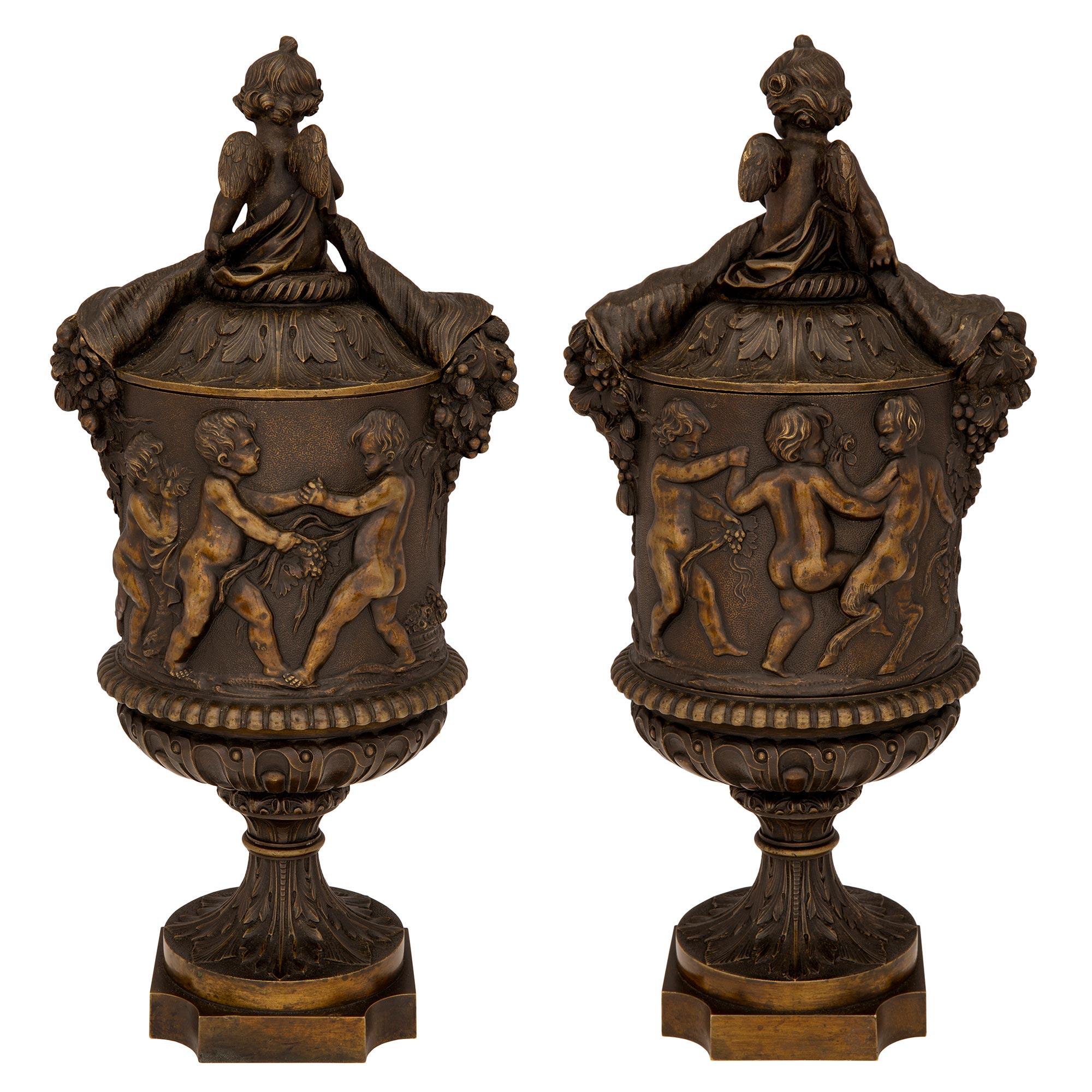 Charmante paire d'urnes à couvercle en bronze patiné de style Renaissance du XIXe siècle, attribuée à Auguste-Maximilien Delafontaine. Chaque urne est surélevée par une base carrée aux angles concaves et un piédestal à socle fin. Les corps