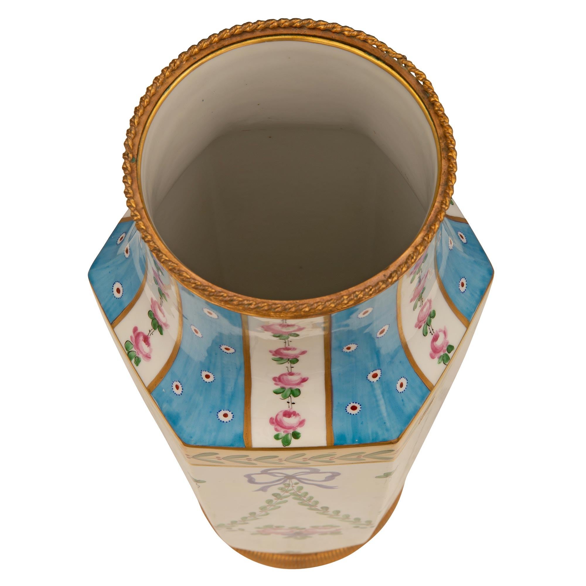 Ein bezauberndes Paar französischer Porzellan- und Ormolu-Vasen des 19. Jahrhunderts aus dem Louis XVI. Jede schöne handbemalte Vase wird von einem fein ziselierten, kreisförmigen Ormolu-Band mit einem schönen Riet- und Lorbeerzweig-Muster gekrönt.