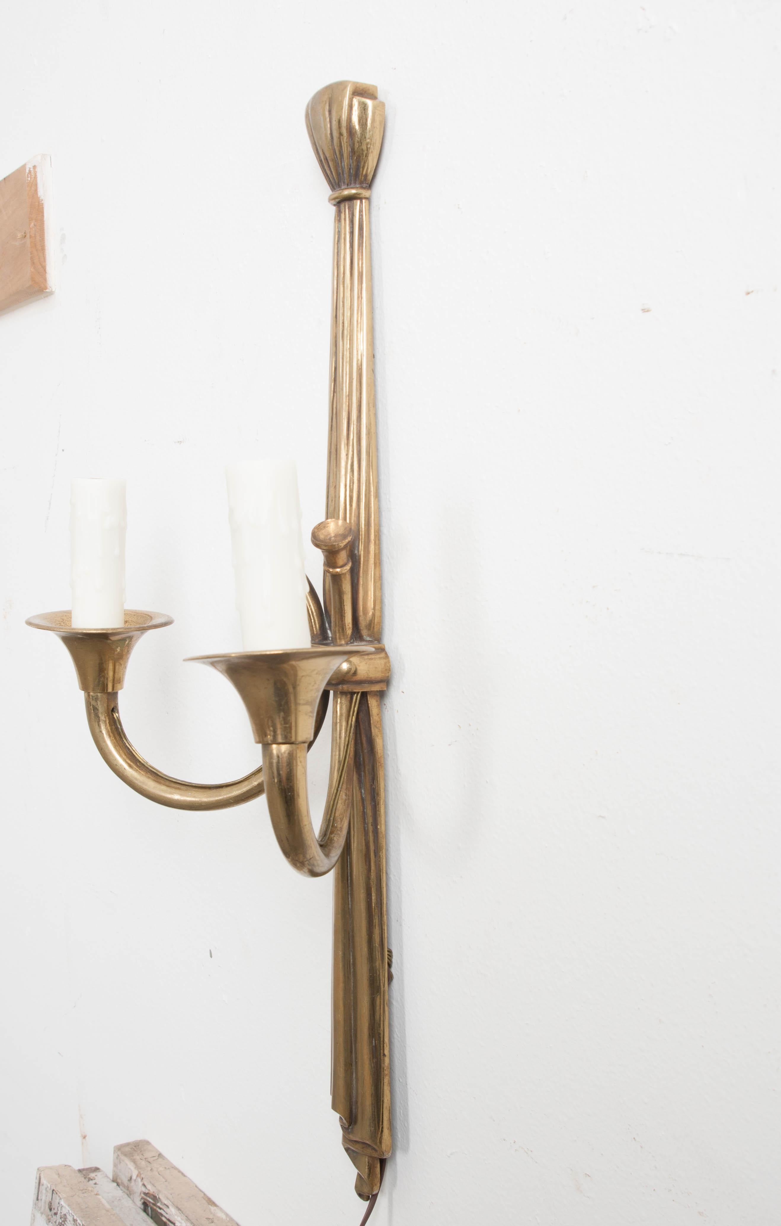 This elegant and weighty pair of Neoclassical-style solid brass double-arm sconces, circa 1880, are from France and feature “draped” standards and Horn-form arms and bobeches. These sconces have recently been outfitted with faux candlesticks and
