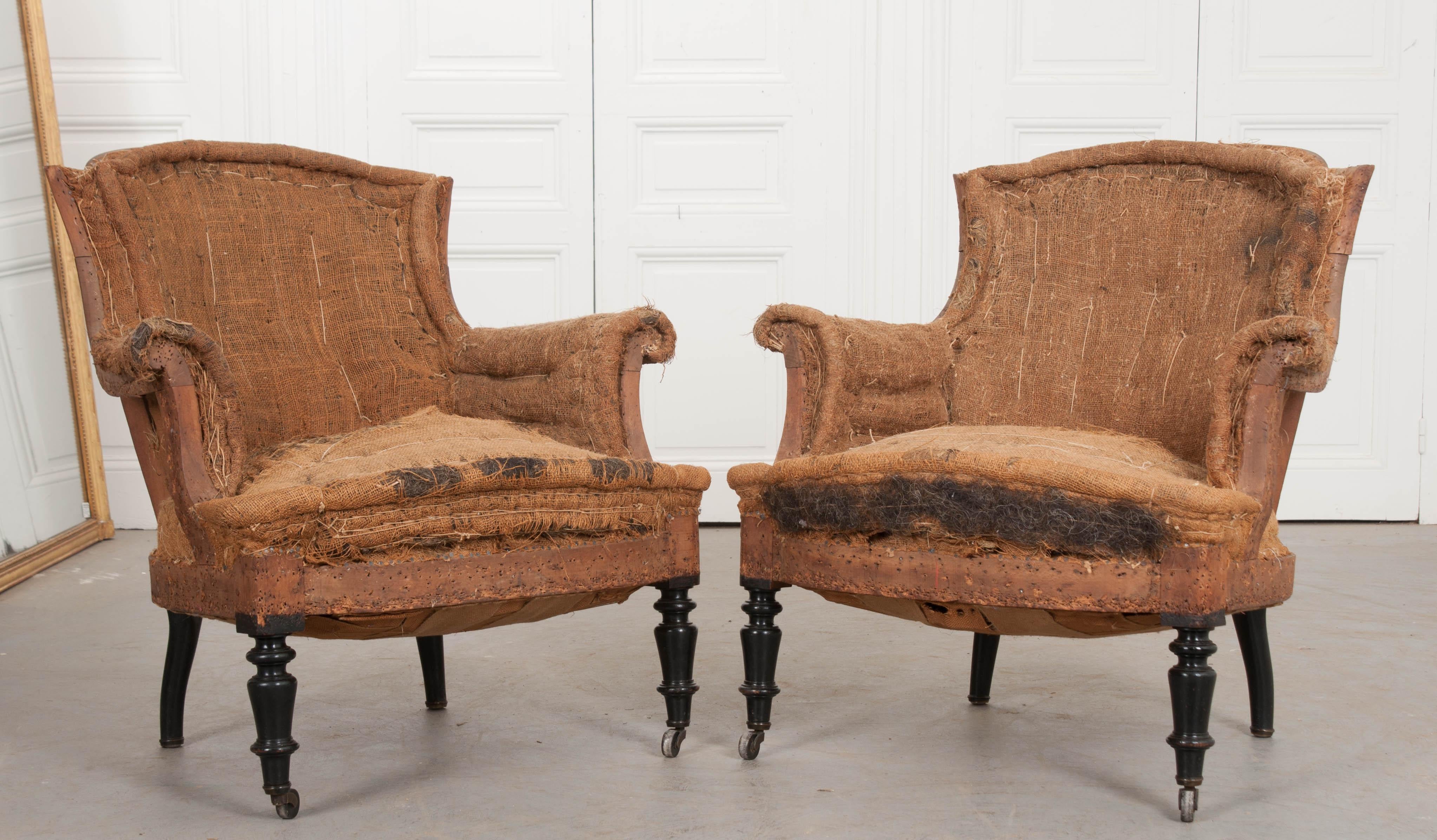 A fantastic pair of structured armchairs, not upholstered, from 19th century France. The pair have a shapely form, with rolled arms and styled back. The chairs are lifted by four ebonized legs, of which the front two have been wonderfully turned and