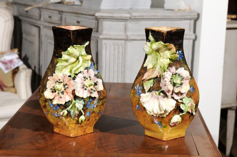 A pair of French faïence vases from the 19th century, adorned with a barbotine décor of applied flowers and leaves. Born in France during the 19th century, each of this pair of vases features a dark brown body evolving into a golden color at the
