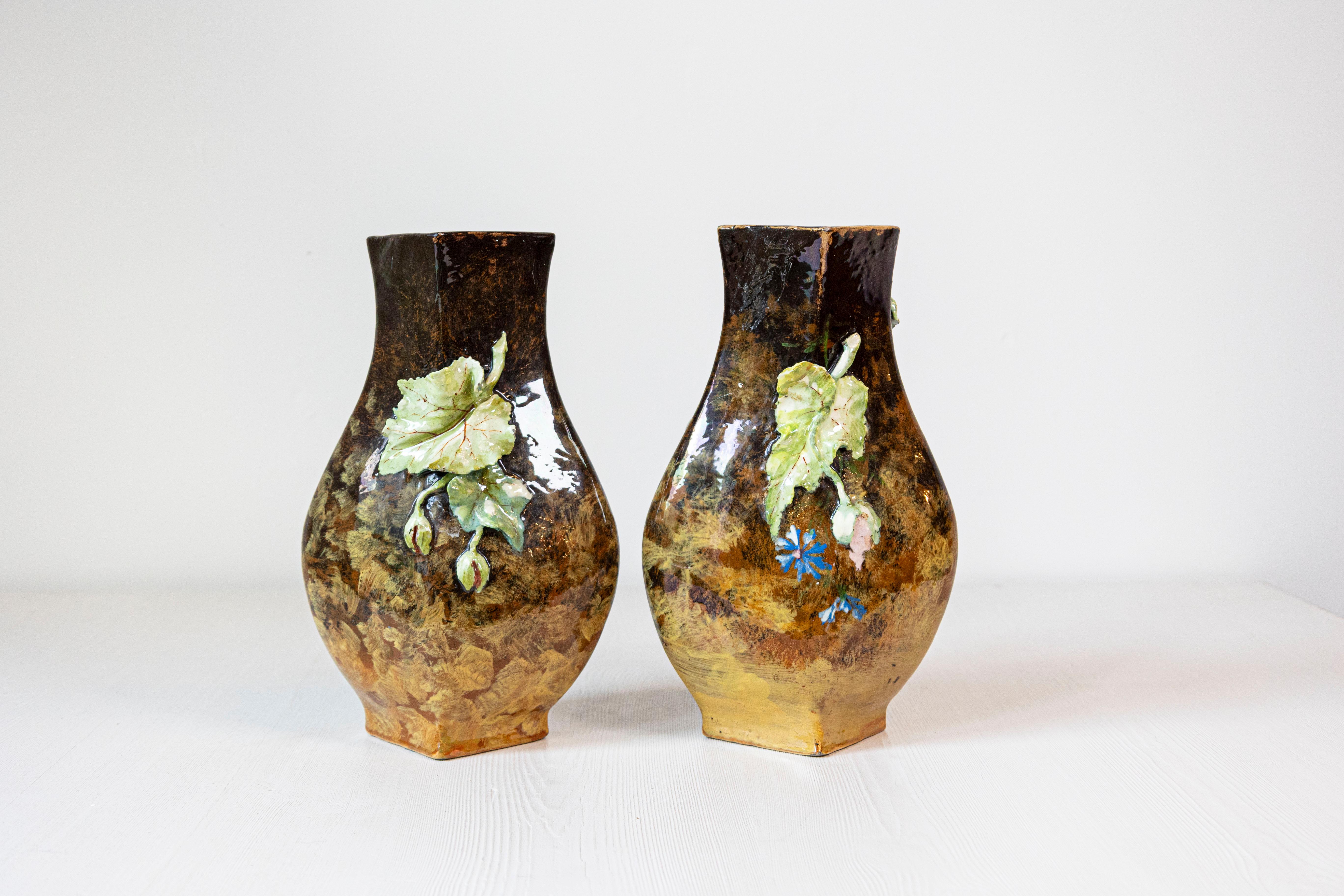 A pair of French faïence vases from the 19th century, adorned with a barbotine décor of applied flowers and leaves. Born in France during the 19th century, each of this pair of vases features a dark brown body evolving into a golden color at the