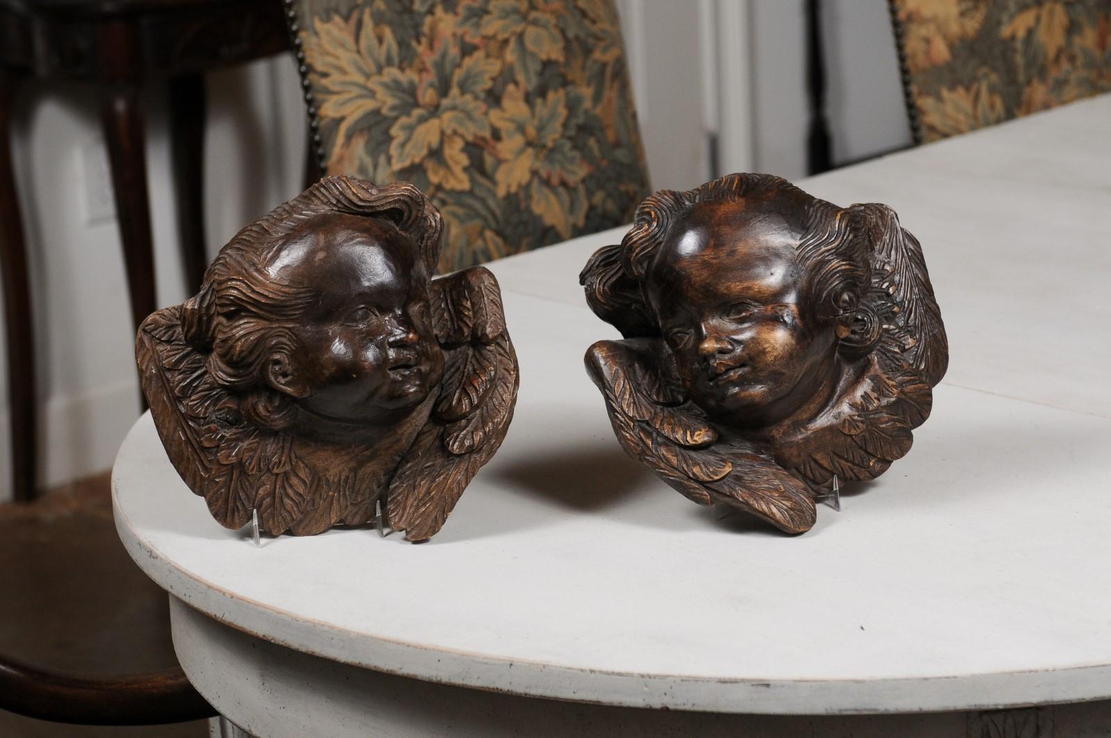 A pair of French walnut wall hanging cherub sculptures from the 19th century, with dark patina. Created in France during the 19th century, each of this pair of nicely carved wall hanging sculptures depicts a chubby cherub face surrounded by