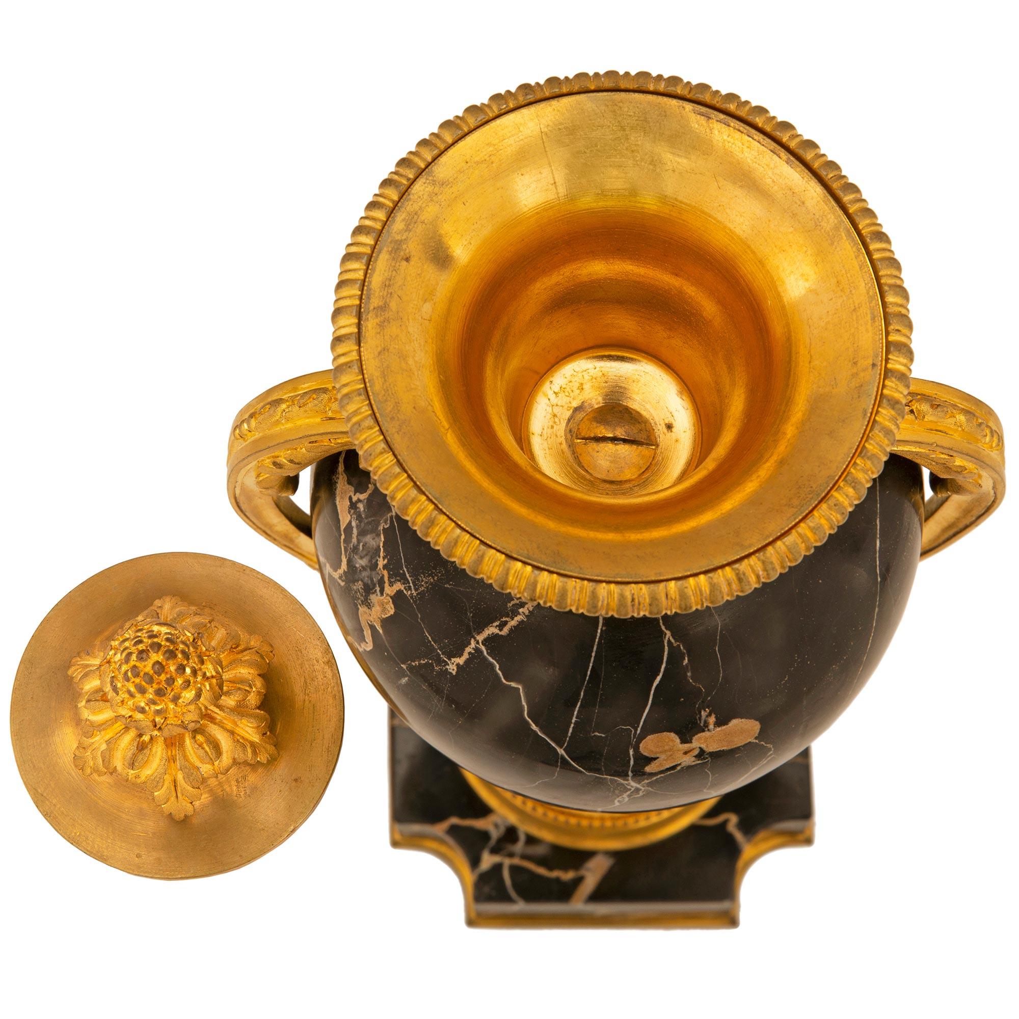 Une belle et très élégante paire d'urnes à couvercle en marbre Portoro et bronze doré de style Louis XVI. Chaque urne est surélevée par une base carrée en marbre Portoro avec des angles concaves et un fin filet de fond en bronze doré. Le support du