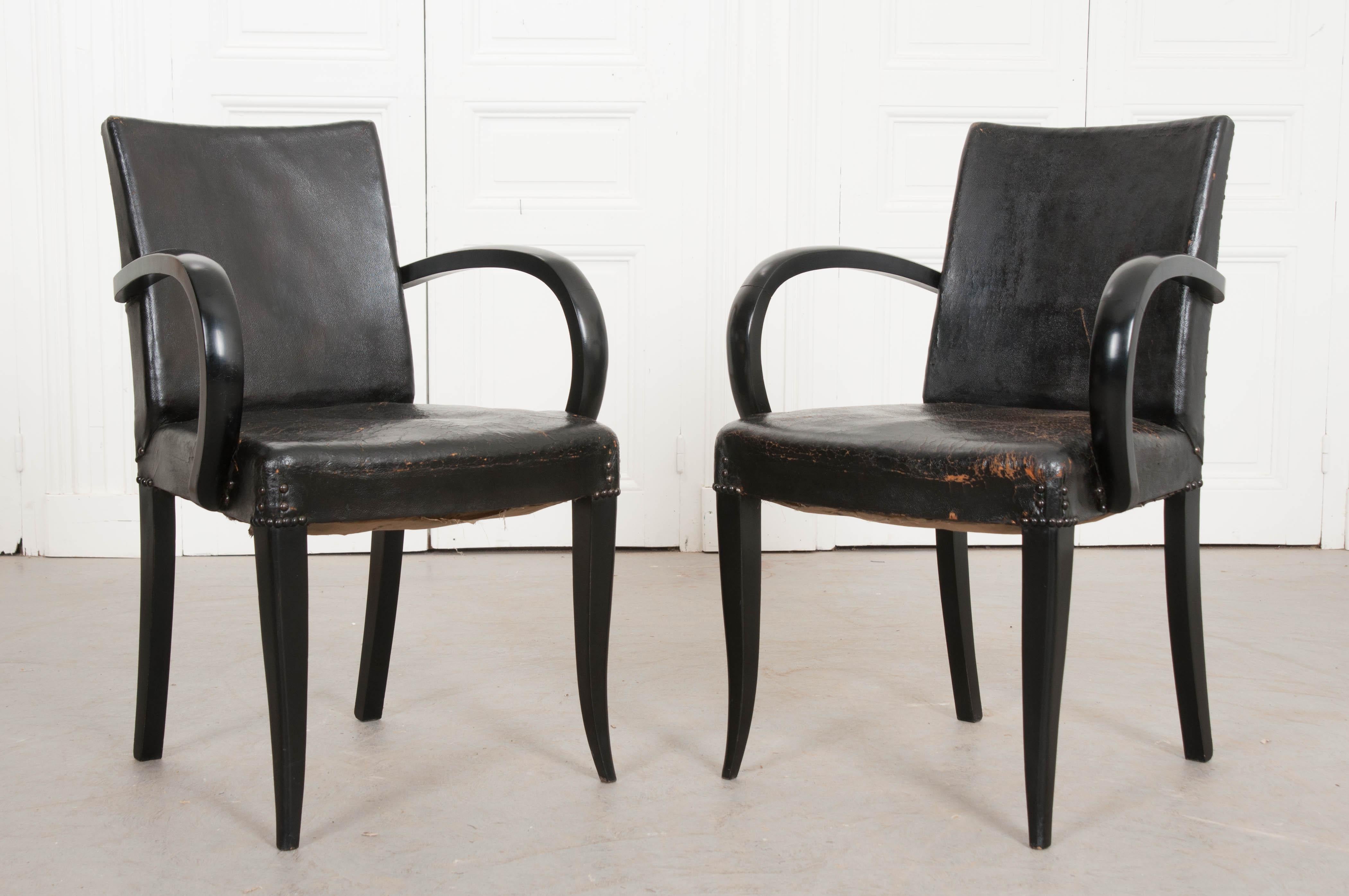 A stylish pair of ebonized Art Deco period armchairs from 1930s France. The chairs have a somewhat simple form, with awesome, arched armrests that take the pair to another level of cool. They are upholstered in their original jet-black leather that