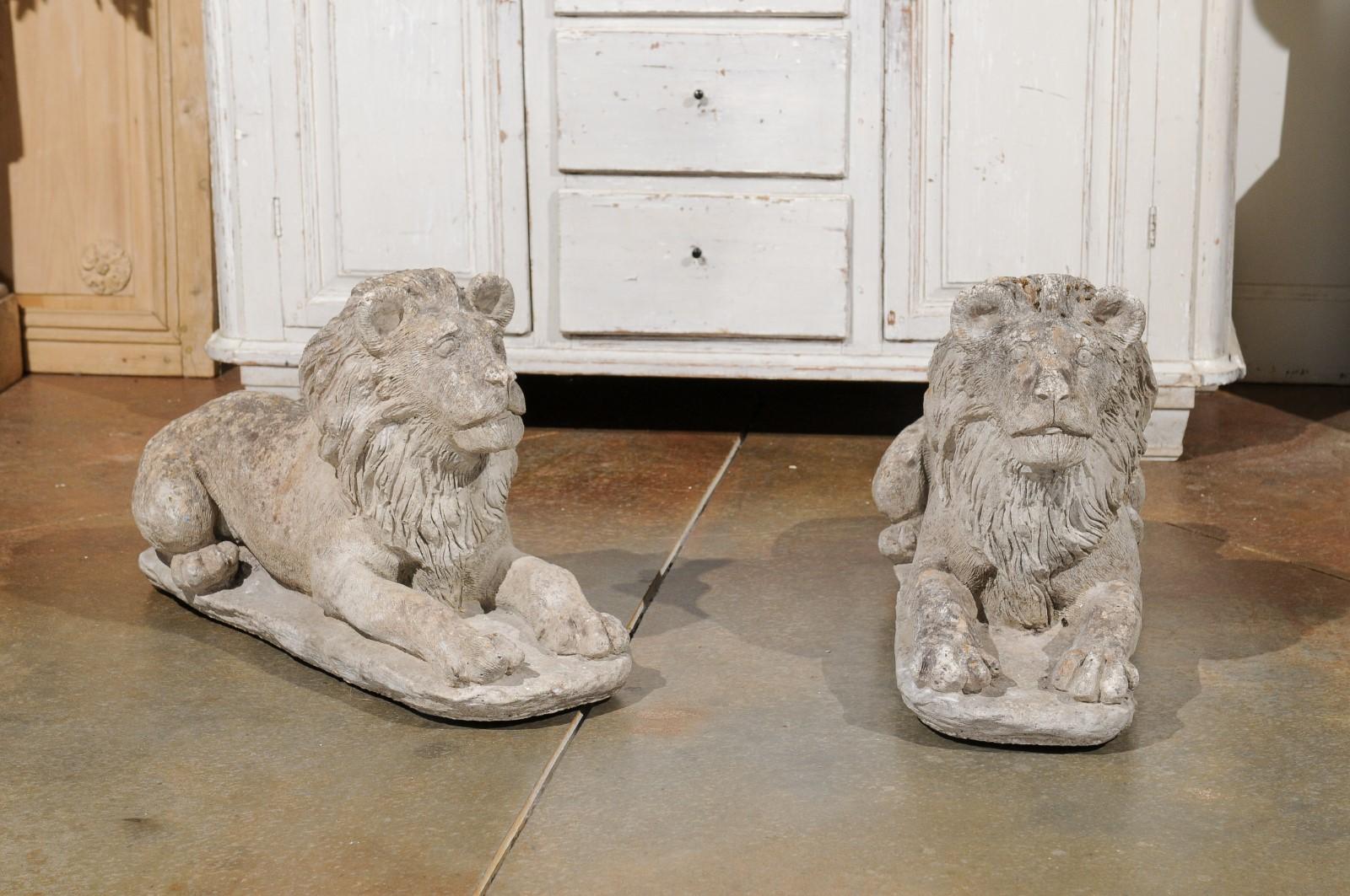A pair of French cement lion sculptures from the 20th century, with weathered patina. Created in France during the 20th century, each of this pair of cement lions charms us with their lovely expression and aged appearance. Reclining and peaceful,