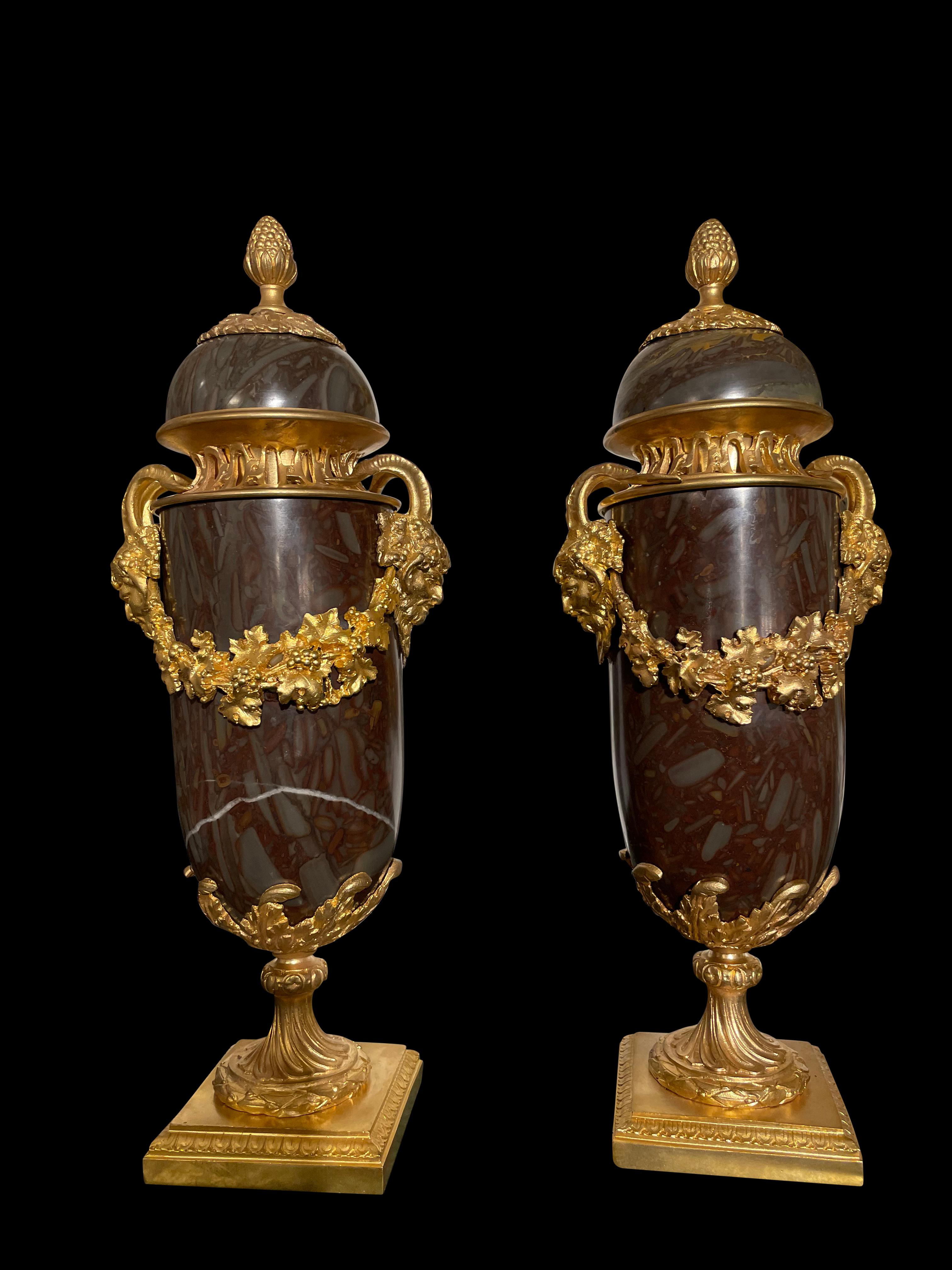 A remarkable pair of French 20th century Louis XVI style onyx and ormolu lidded urns. Each urn is raised by a square ormolu base with concave corners and a delicate Coeur de Rai wraparound band. The socle shaped pedestals display fine wraparound
