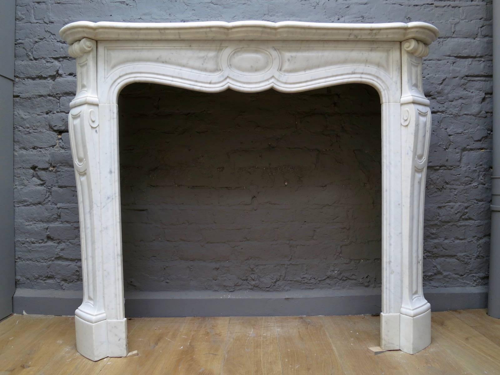 A pair of pompadour style fireplaces in the manner of Louis XV, carved in Italian Carrara marble. One slightly larger than the other. The frieze with moulded design and plain centre medallion. The cantered panelled jambs with scrolled end blocks,