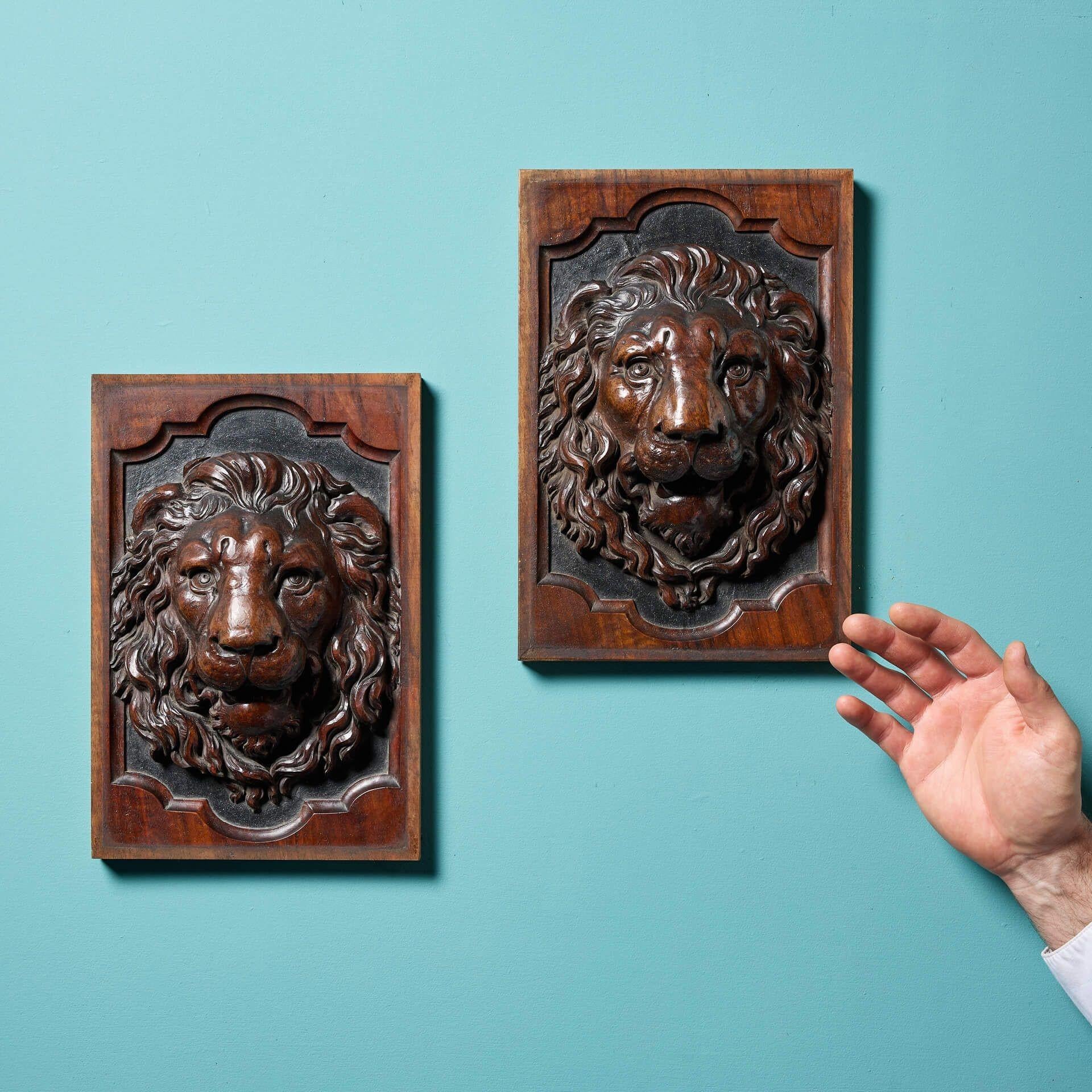 A handsome and beautifully carved pair of matching English antique lion panels, circa 1870. Each walnut panel depicts the mask of a commanding lion, very deeply carved in relief with abundant, flowing manes and teeth bared. Place either side of a
