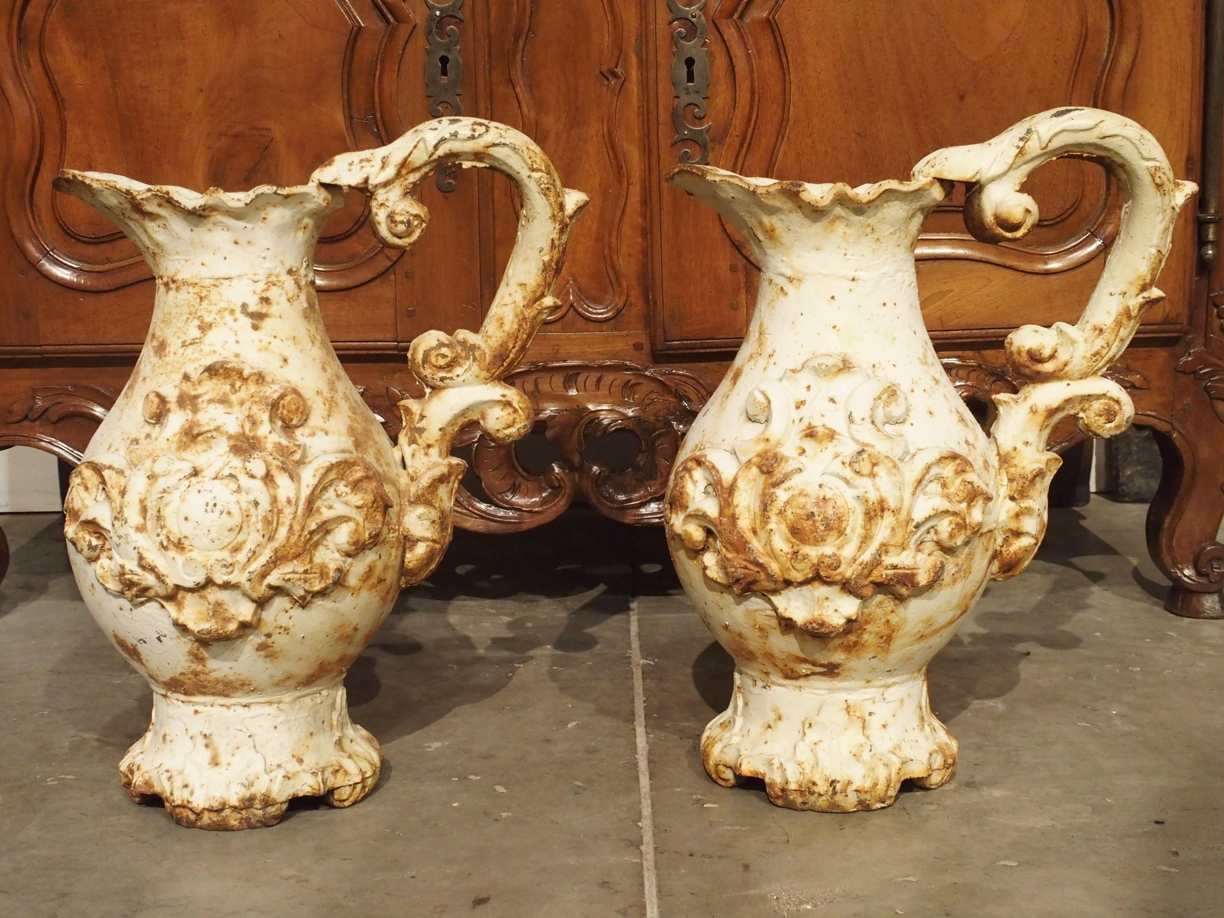 This pair of large antique French parcel paint pitchers has very ornate designs. In the Rococo style, their motifs are drawn from nature. Their scalloped upper rim imitates the shell motif and their handles are acanthus leaf C-scrolls. The shaped