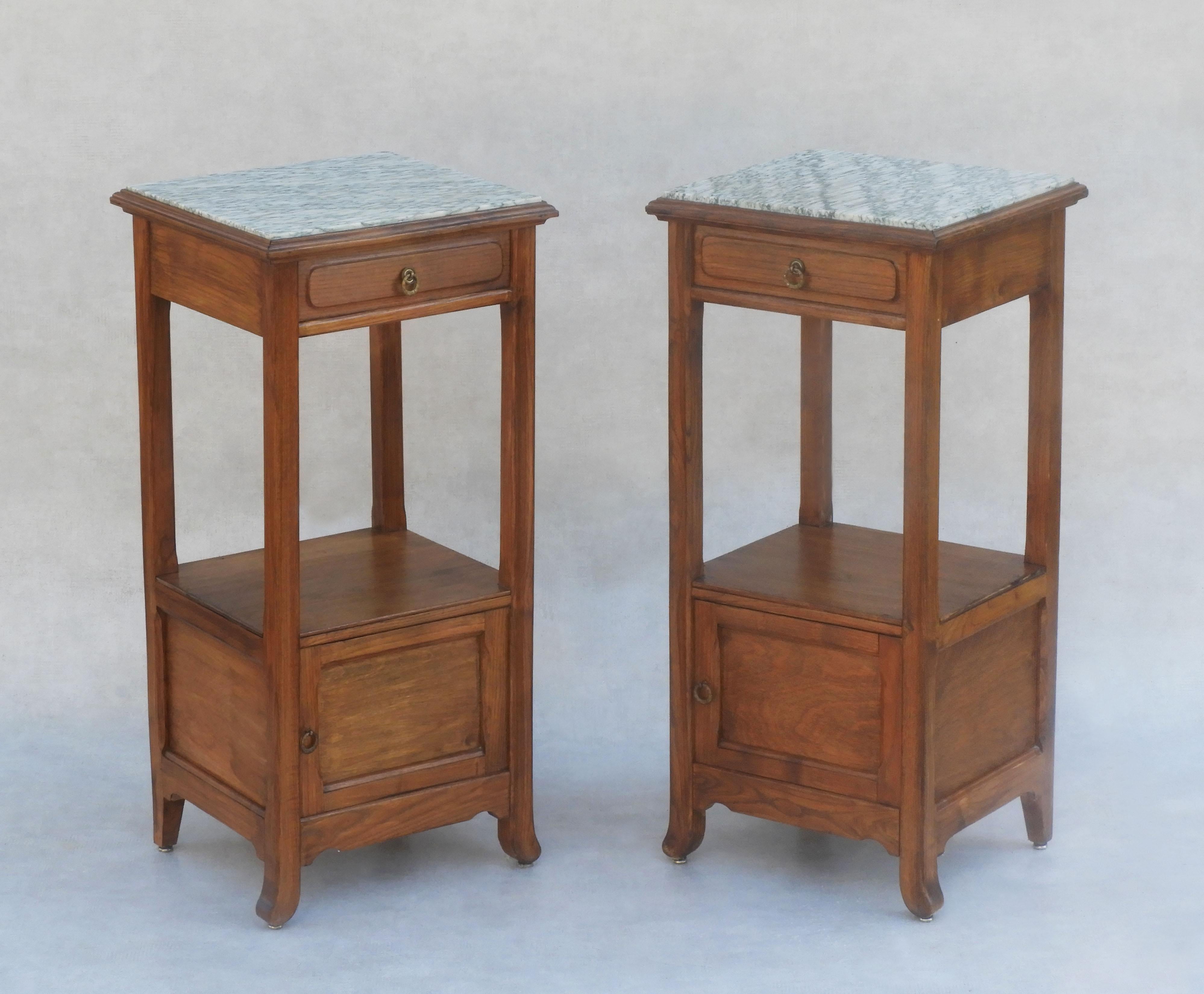 A fabulous pair of oak bedside tables or nightstands from 19th-century France. Two stylish cabinets each with a shelf, drawer and cupboard. Tall, slim and generously proportioned with an attractive off-white and grey-green variegated marble top and