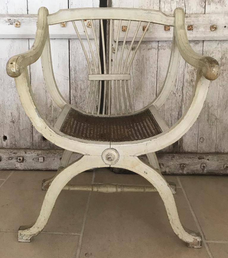 Unusual early 1900s French antique pair of armchairs in original white paint with carved backs and beautiful curved arms and legs. They hark back to Napoleon's favorite Empire style and are very delicate to look at.

Canework seats complete the